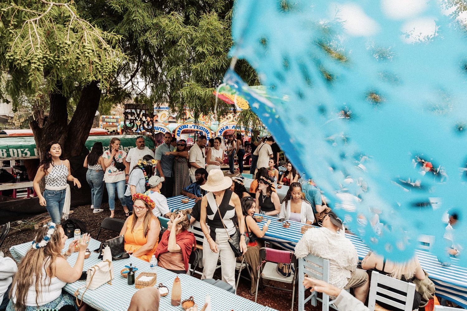A crowd gathers at an outdoor restaurant patio with a bright blue banner or decoration blowing in the wind.