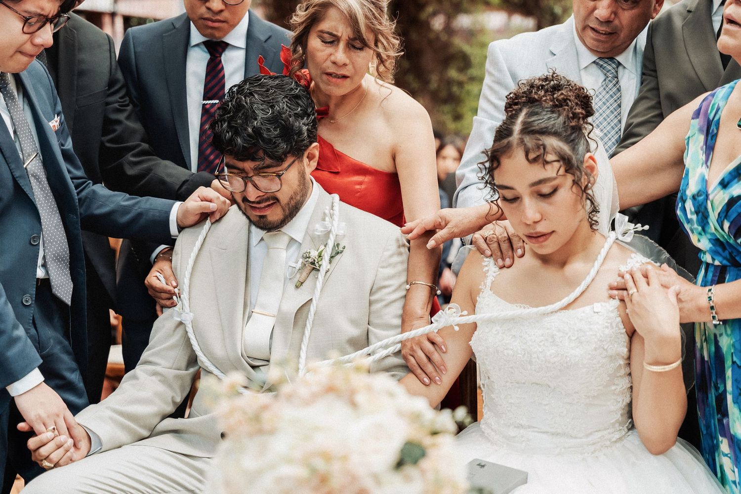 A couple is overcome with emotion during a wedding ceremony while seated among guests in formal attire.