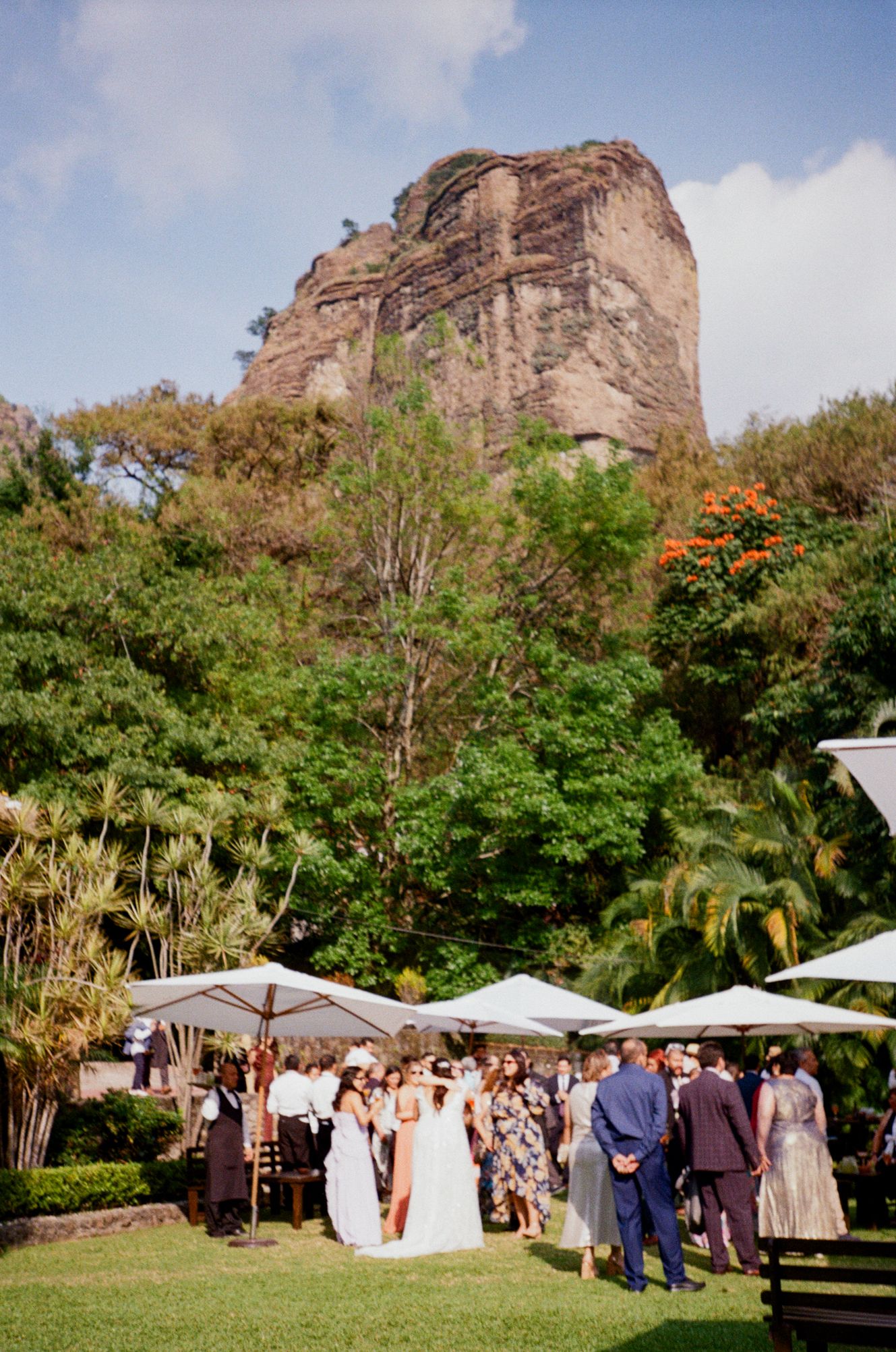 Panoramic view of an outdoor wedding ceremony setup with white umbrellas against a dramatic rocky cliff backdrop.