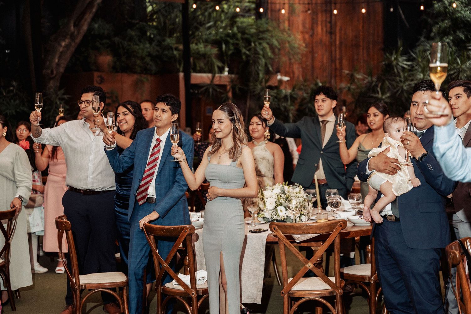Wedding reception guests seated at long tables enjoying dinner under string lights.