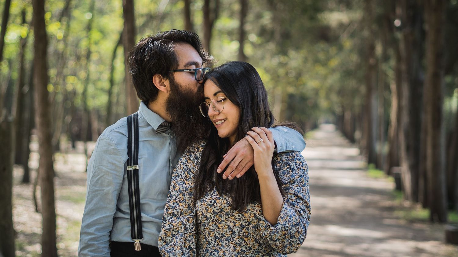 A tender moment shared between a couple on a tree-lined path.