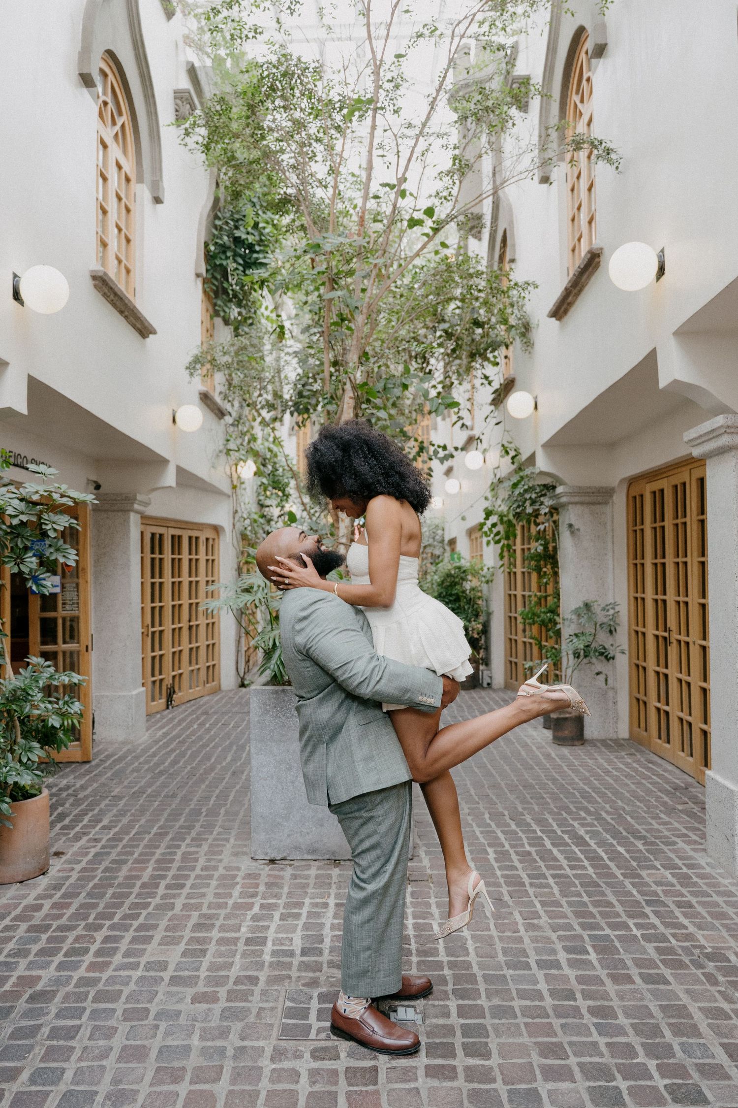 A couple embraces and spins in a romantic dance sequence across a stone courtyard with white walls and greenery.