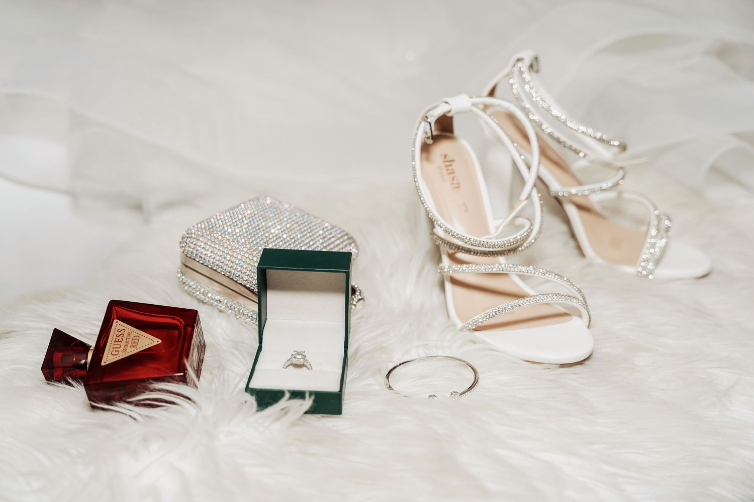 Wedding accessories including strappy heels, rings, and jewelry arranged on white surface.