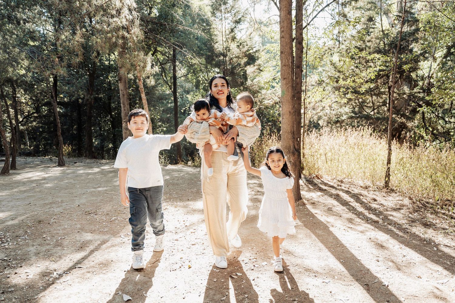 A sunny forest path with people walking together on a dirt trail surrounded by tall pine trees.