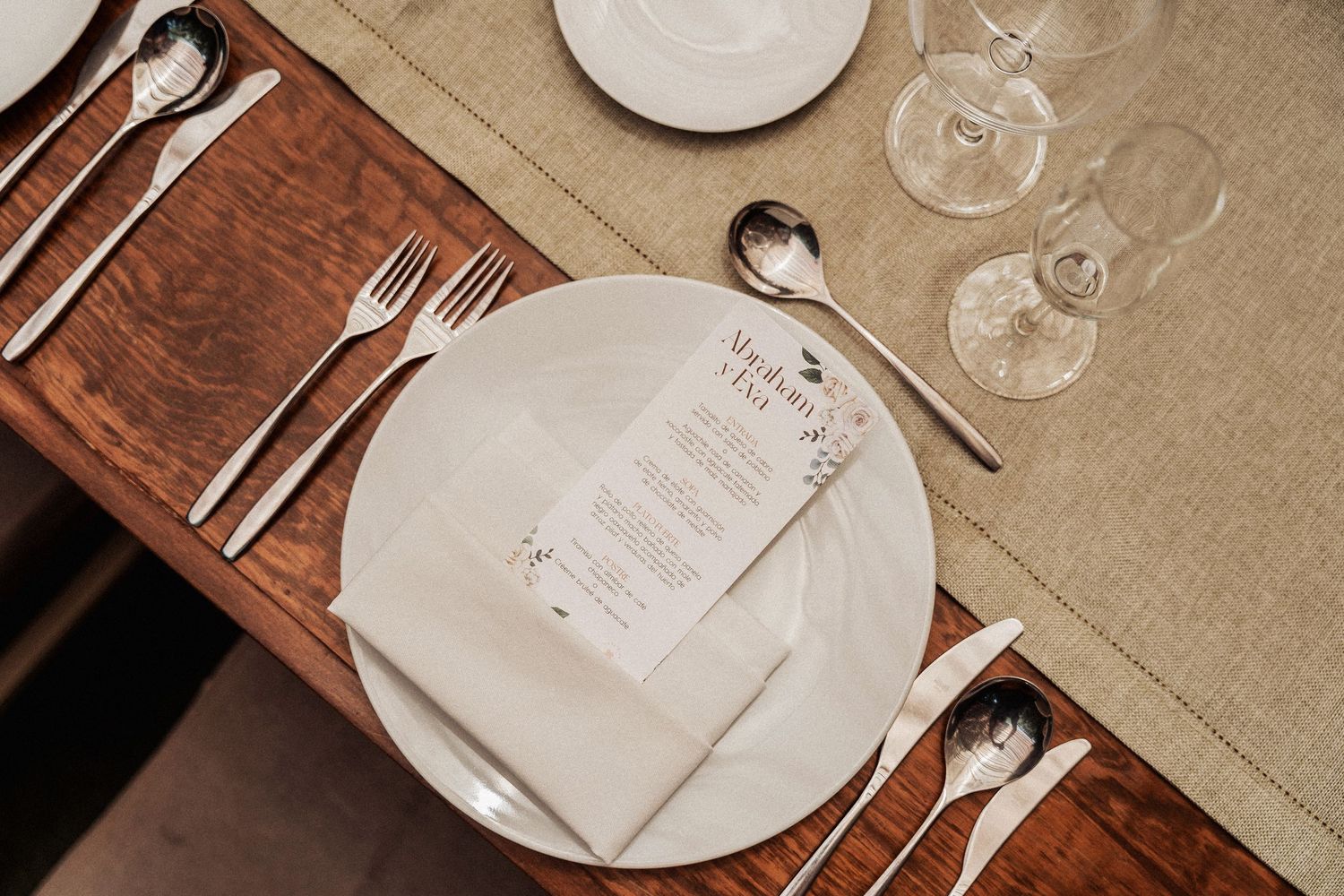 Place settings featuring white plates and wine glasses arranged on neutral linen tablecloths in a warm restaurant setting.