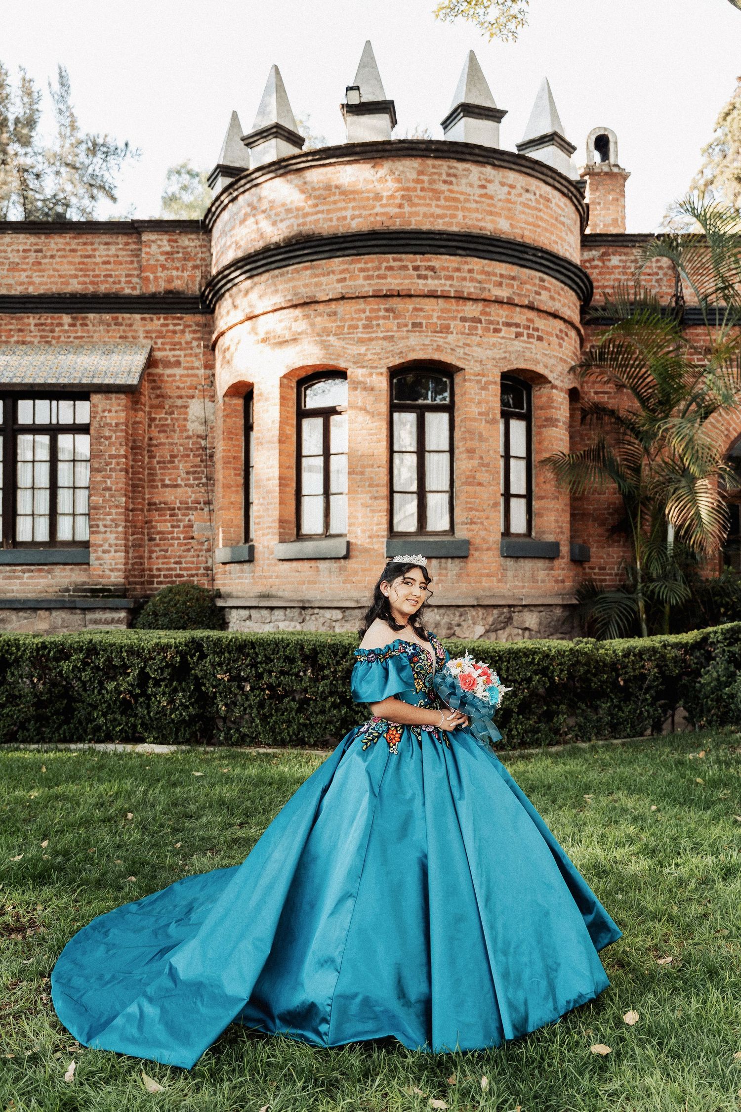 Beautiful teal ballgown photographed at a historic brick manor with ornate turret architecture and manicured gardens.
