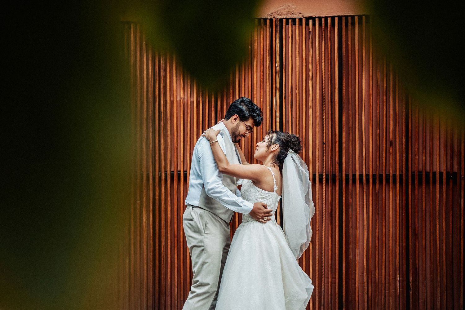 Intimate wedding portraits captured against a wooden wall backdrop with dramatic lighting.