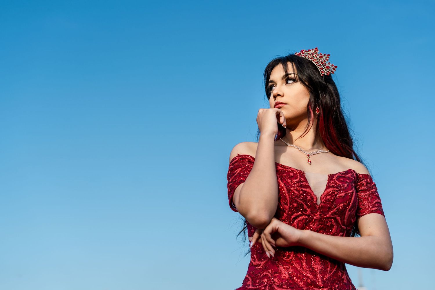 A person wearing a red sequined dress poses gracefully against a blue background for a modeling photoshoot.