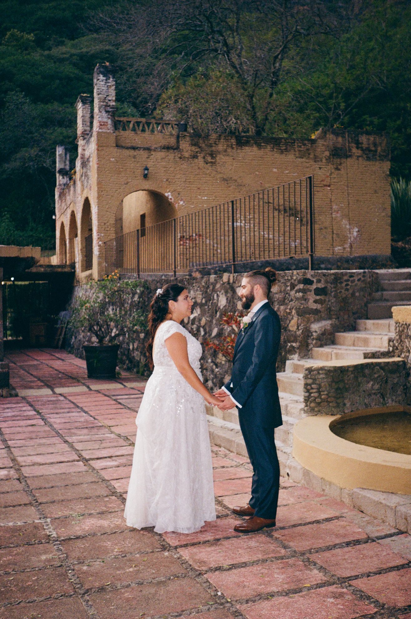 A couple shares an intimate moment on a rustic terrace with stone walls and pink tiled flooring at sunset.
