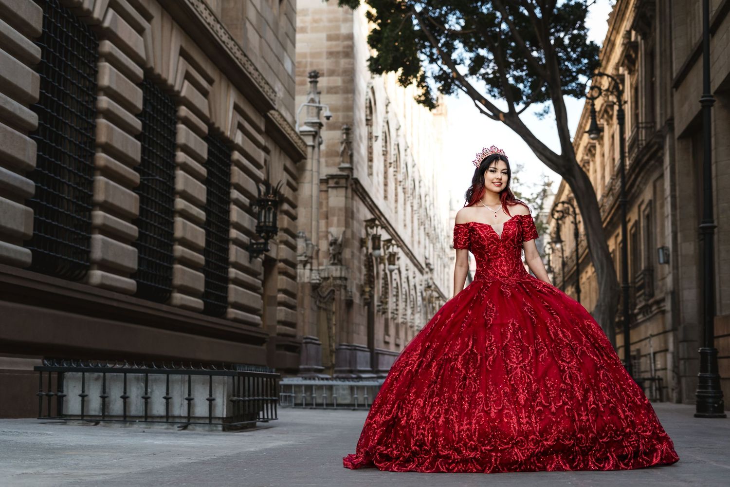 Elegant red ball gown with sequins sparkles in an ornate European city street with historic architecture.