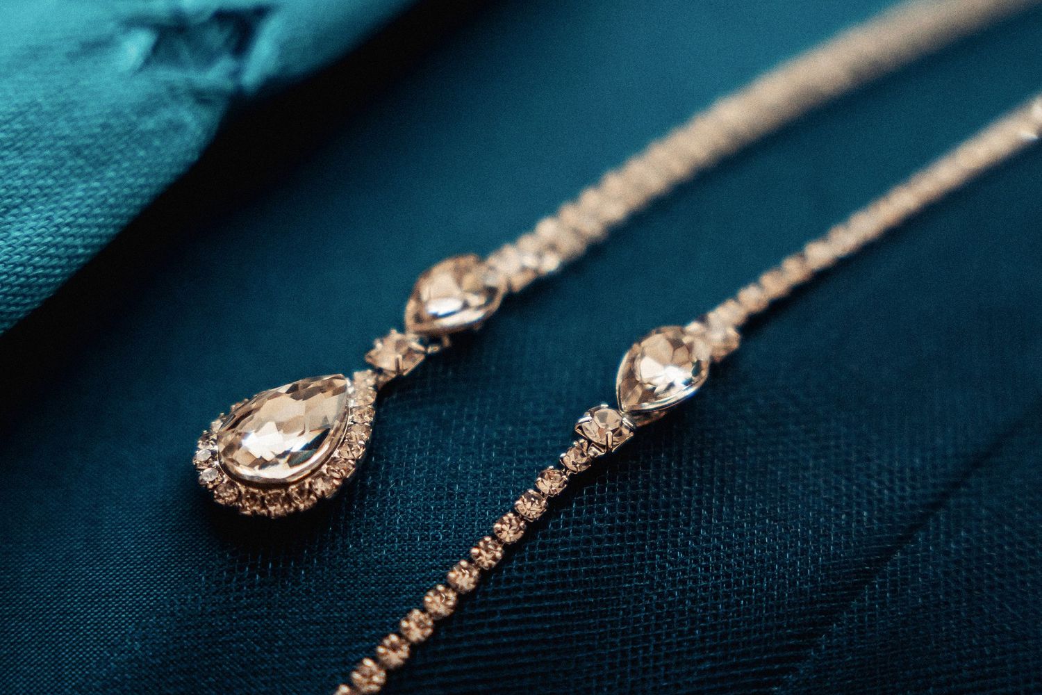 Elegant rose gold teardrop necklace with crystal details on a teal fabric background.
