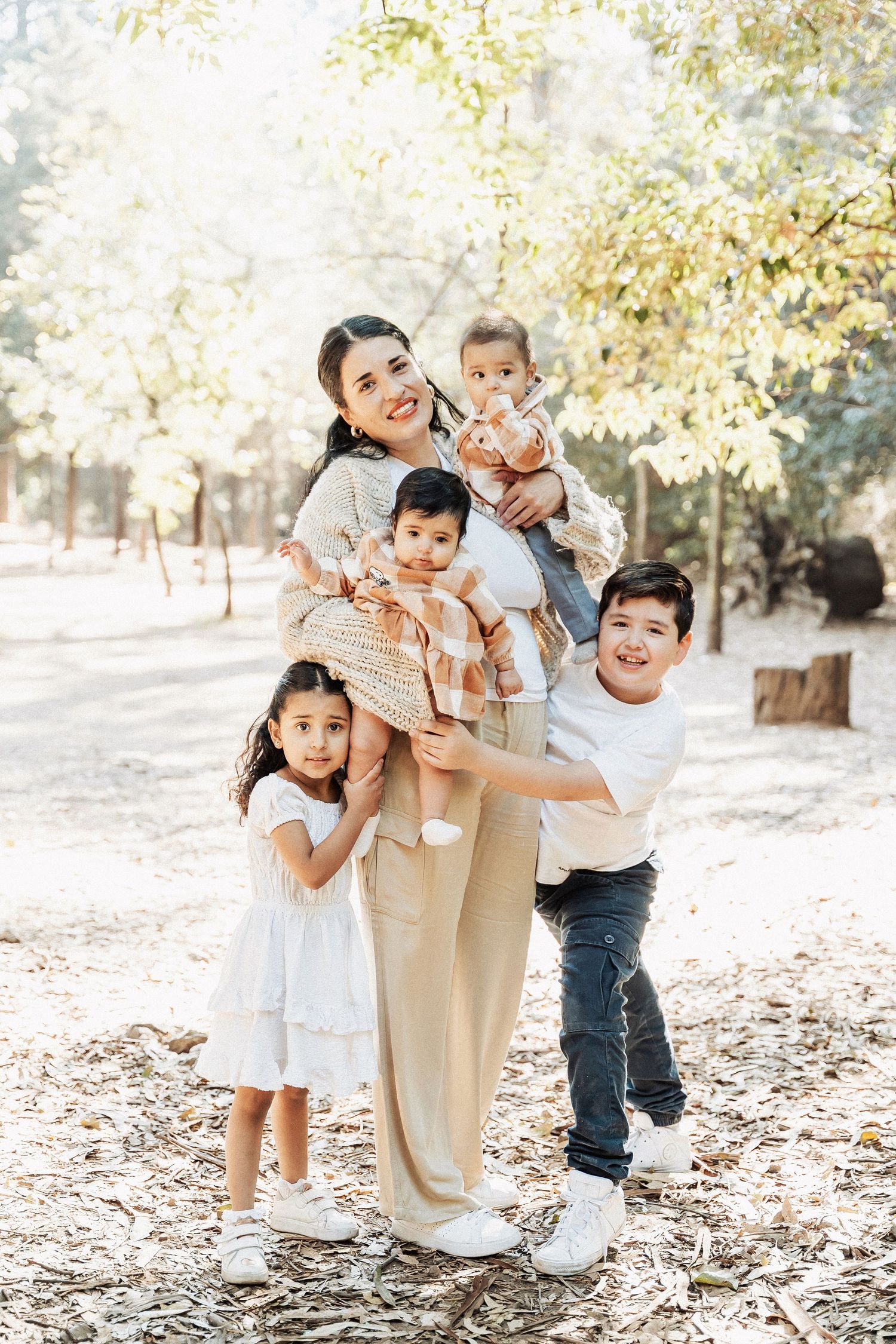 Family group smiles joyfully while posing together in a sun-dappled outdoor park setting.