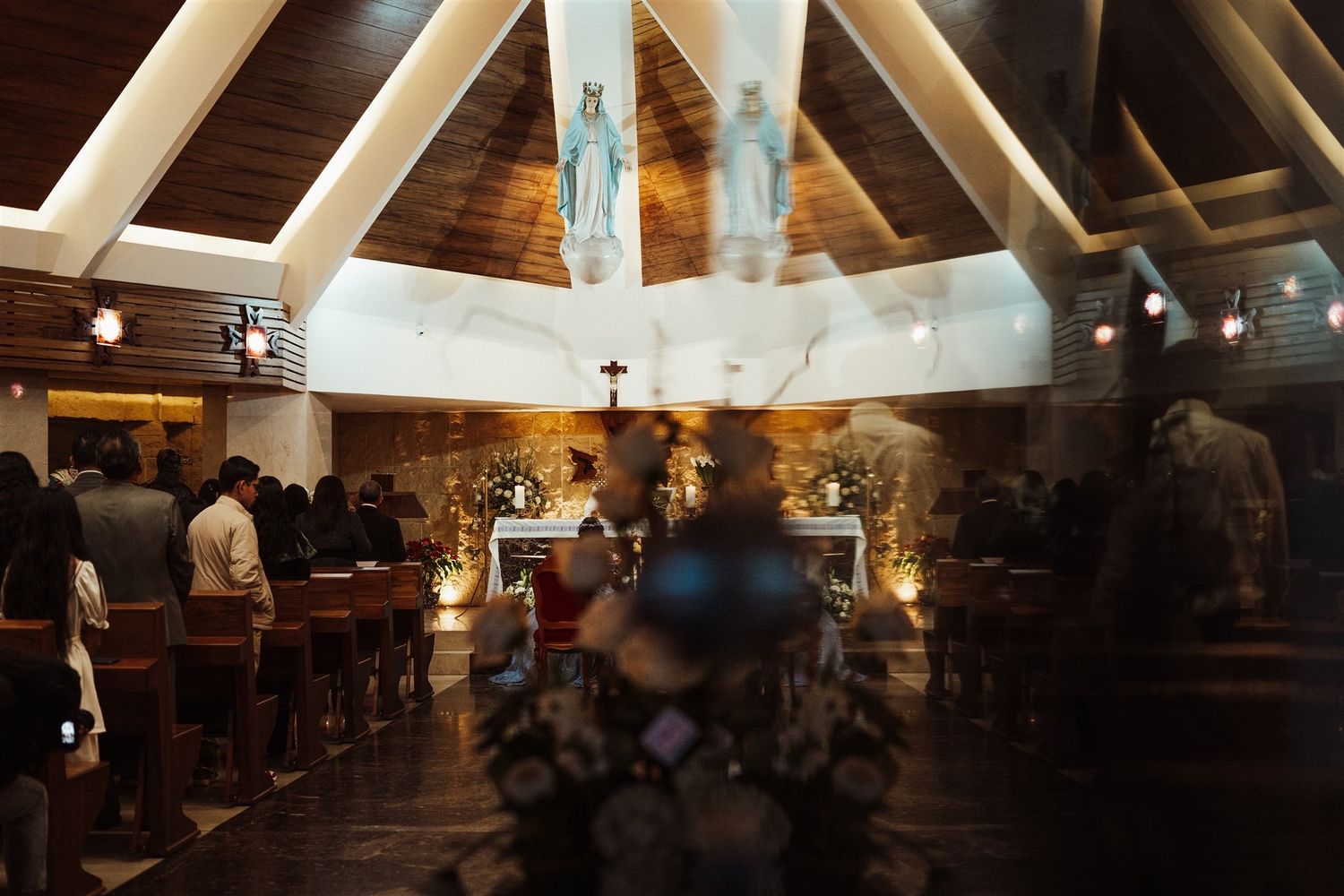 A Catholic church sanctuary with wooden beams and skylights glows warmly during an evening mass service.