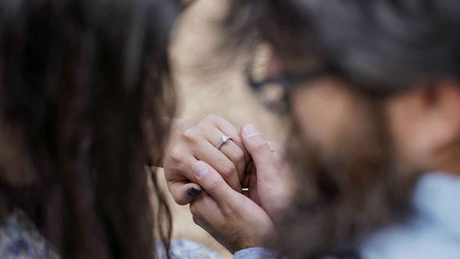 Close-up of hands showing an engagement ring in soft focus.