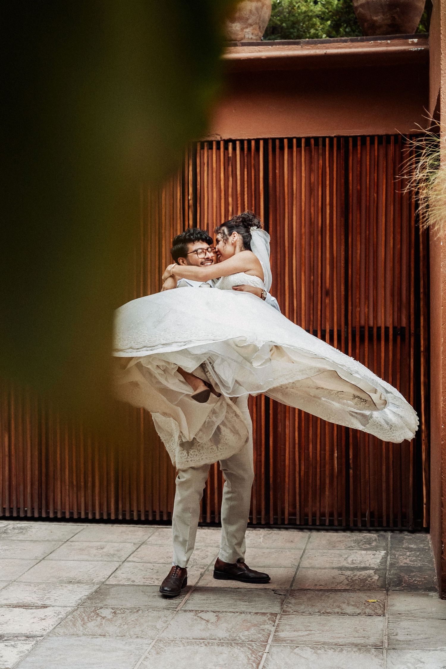 A romantic wedding moment captured against wooden slats with flowing white dress fabric.