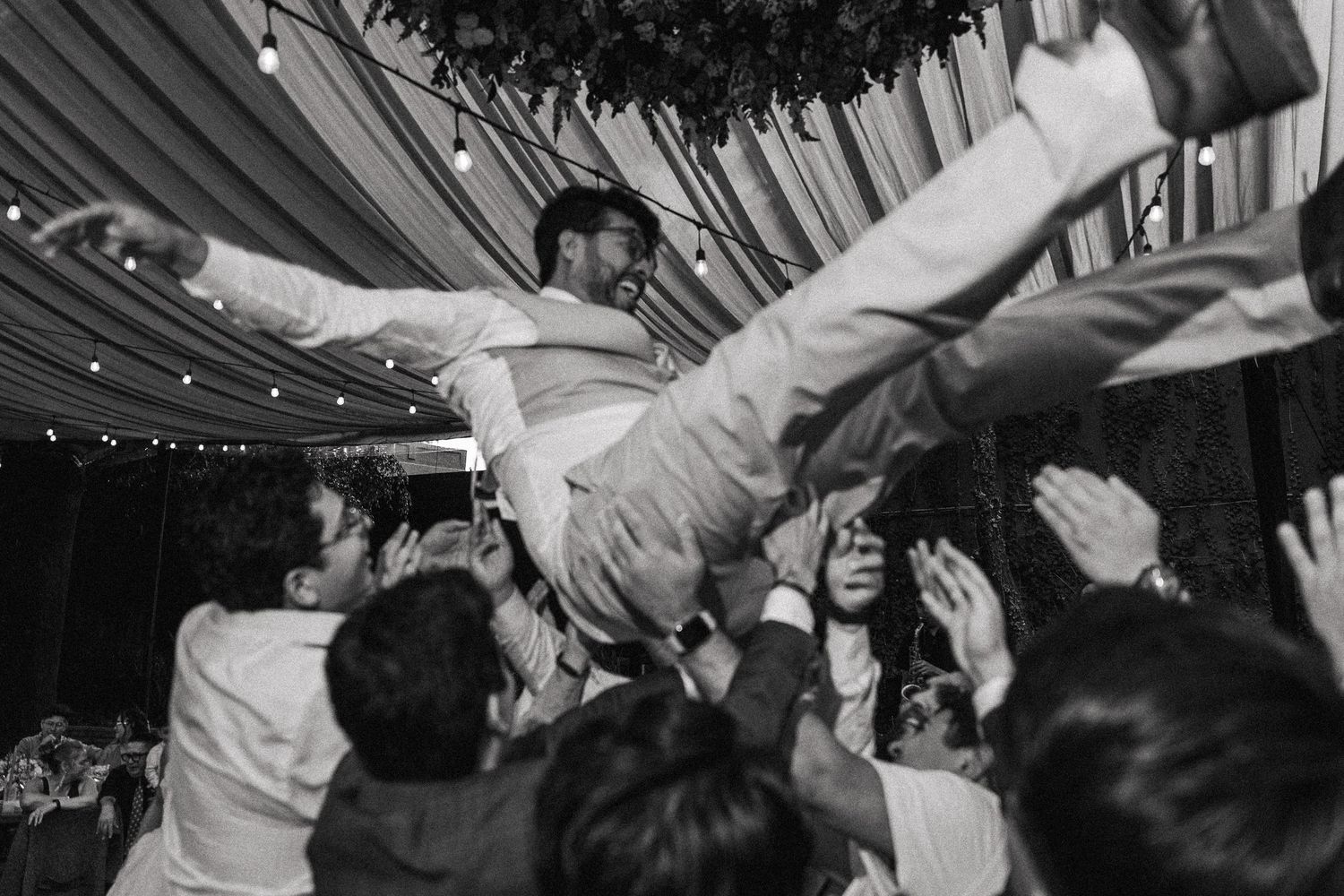Wedding guests lifting someone in celebration during reception party.