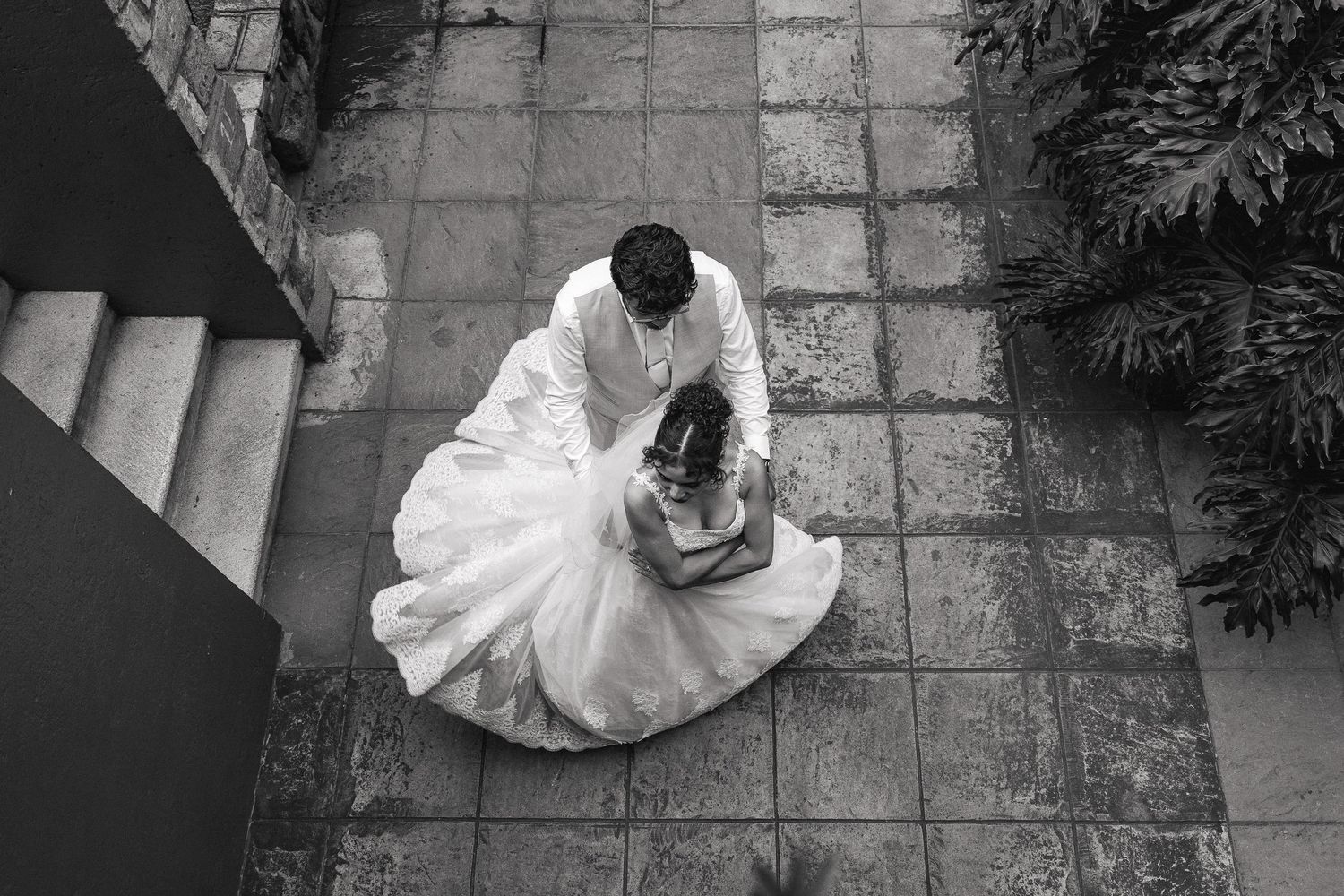 Black and white overhead shot of couple in wedding attire dancing on stone patio.