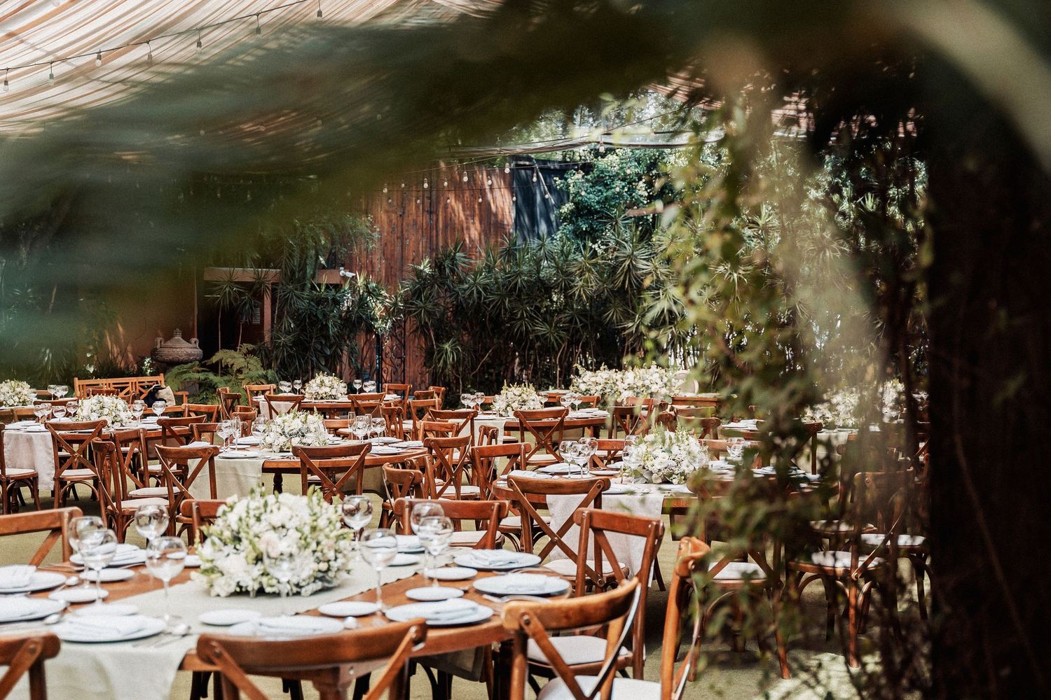Rustic outdoor wedding reception tables decorated with white linens and floral centerpieces under string lights.