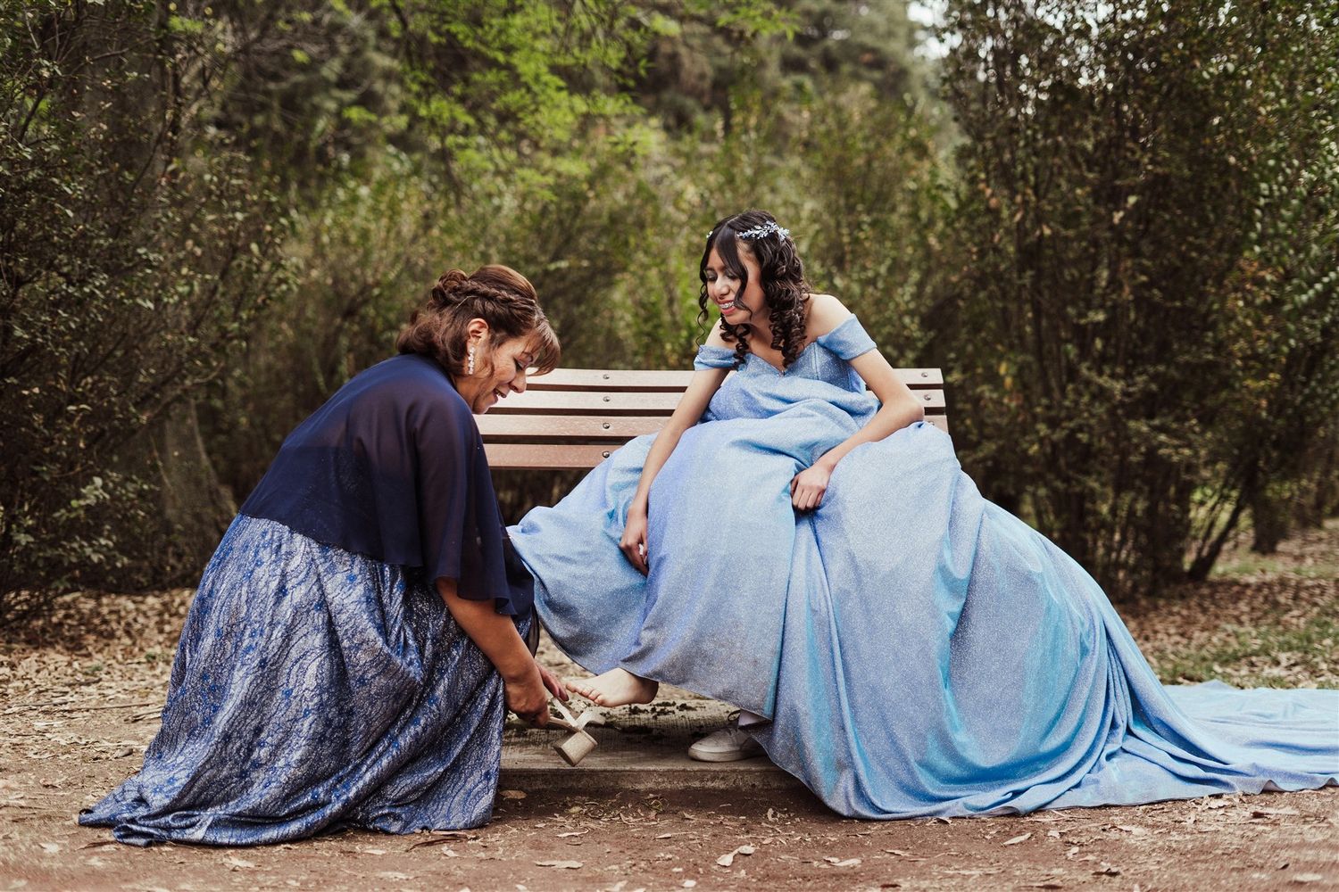 Two figures in elegant ball gowns, one navy and one light blue, pose together on rustic steps in a garden setting.