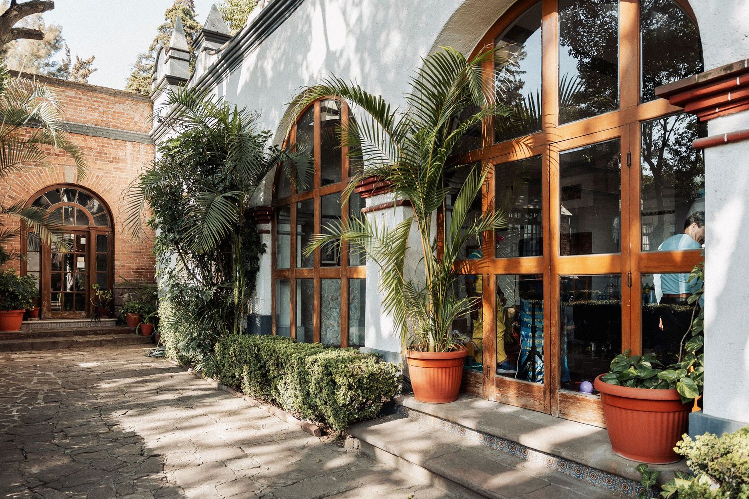 Mediterranean style courtyard with potted palm trees along storefronts features warm stone walls and rustic architecture.