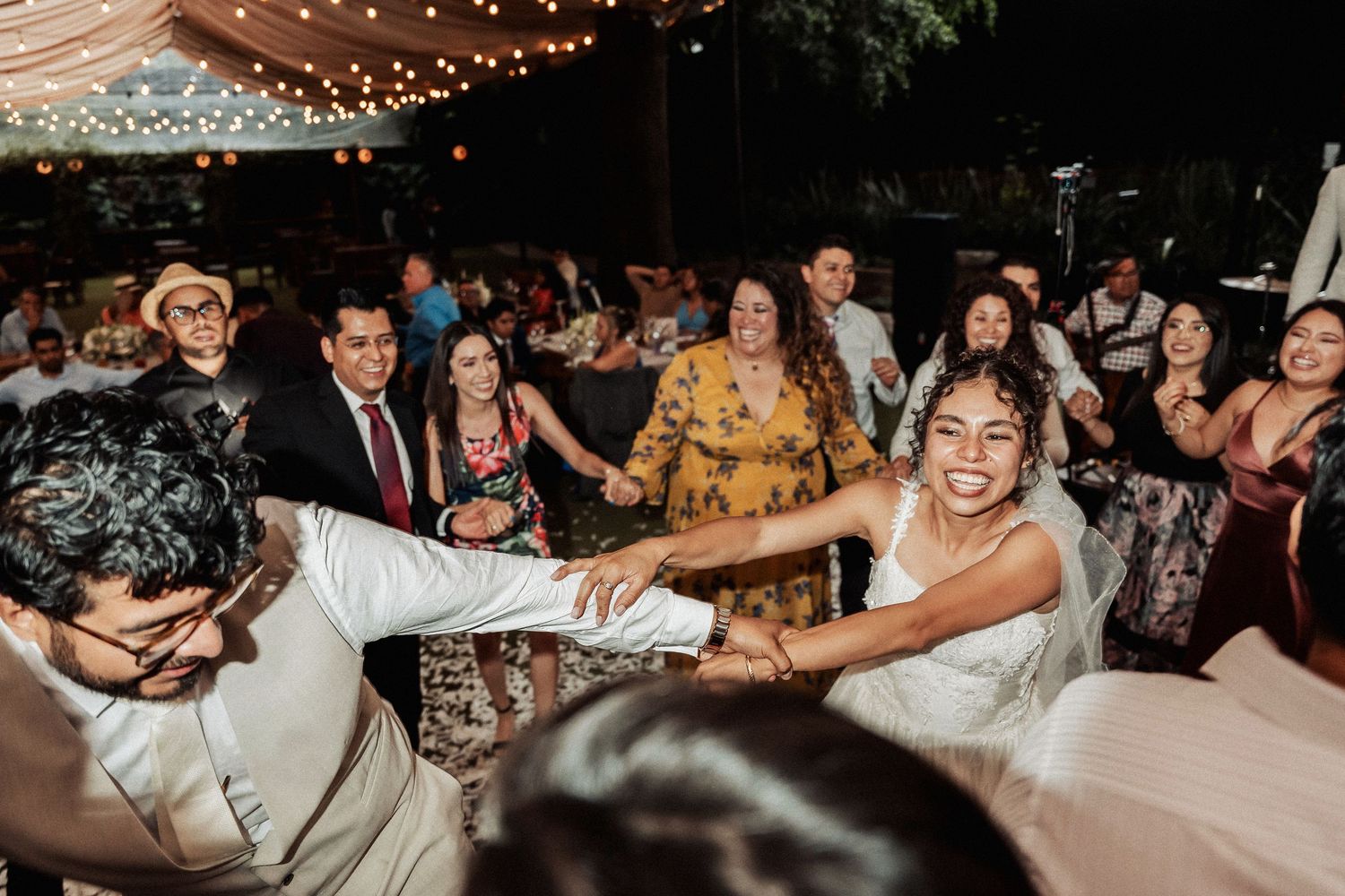 Wedding guests dancing and celebrating on a dimly lit dance floor with string lights overhead.