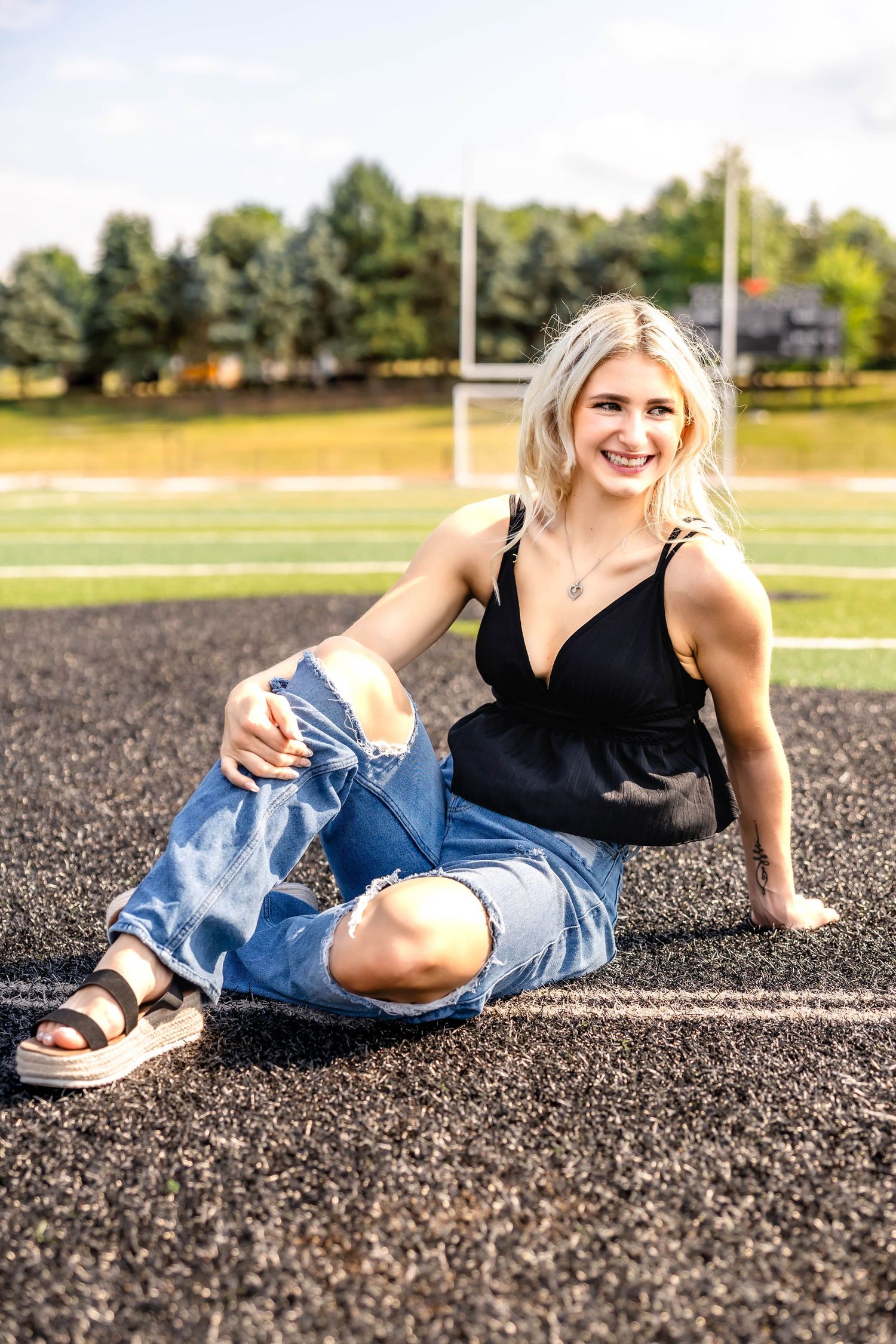 A person in distressed jeans and black top poses casually on a track field.