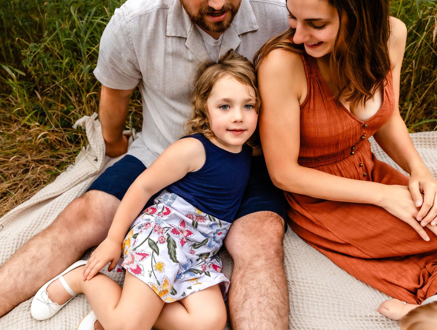 Intimate family moment captured on a blanket outdoors showing genuine laughter and joy.