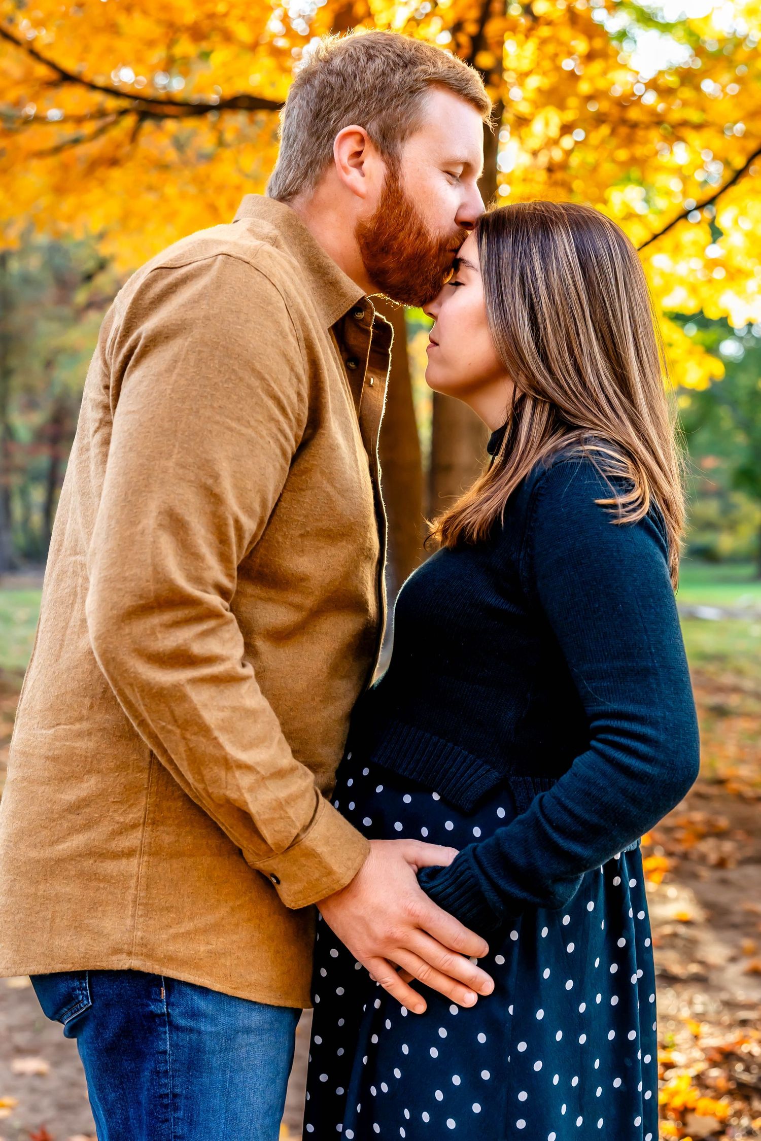 Happy expecting couple embracing under vibrant yellow fall trees.