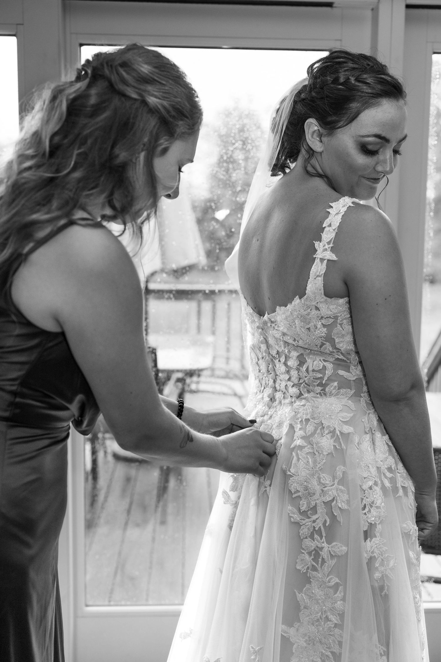 Helper assisting with the back buttons of an intricate lace wedding dress.