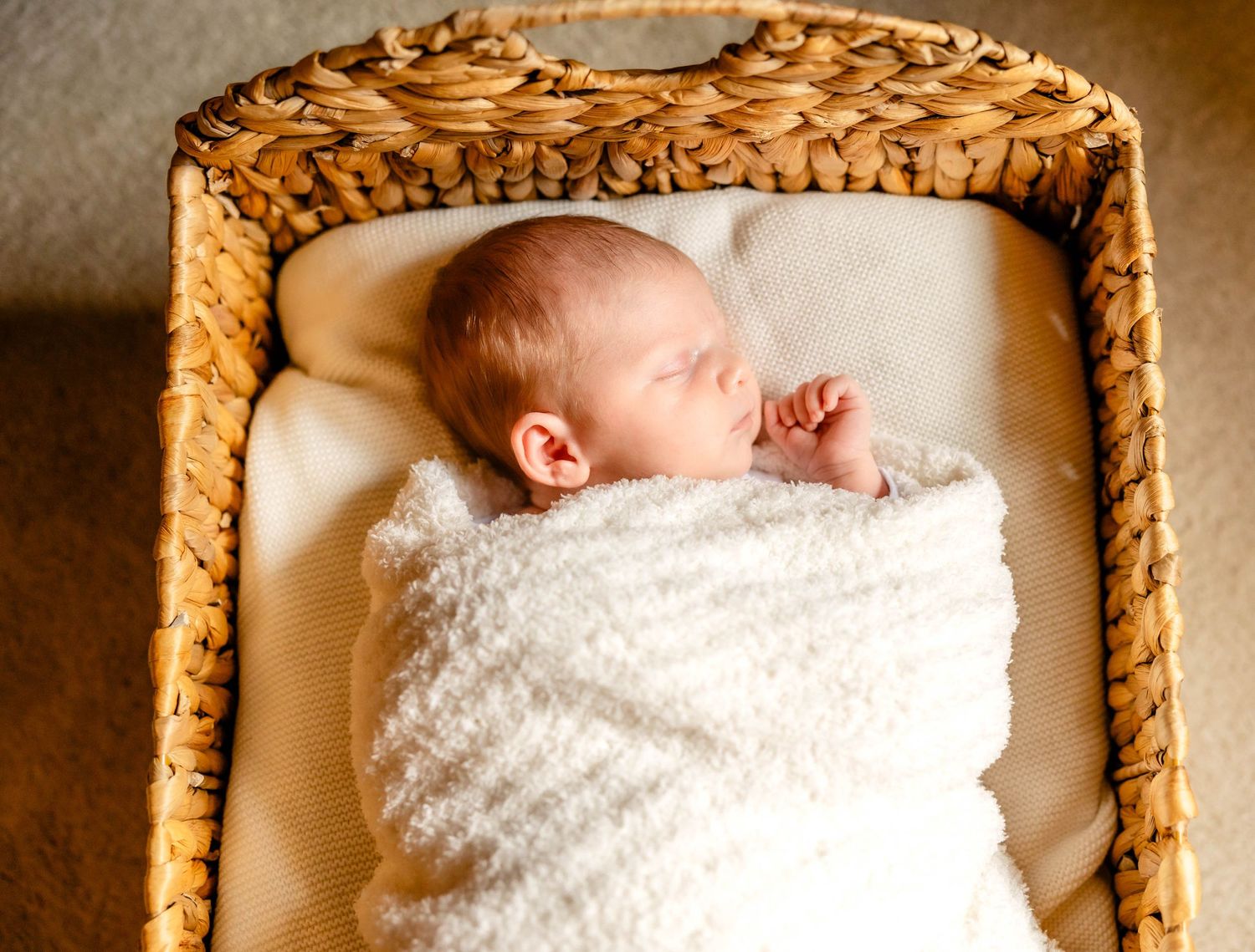 Sleeping infant nestled in cozy white blanket inside rustic woven basket.