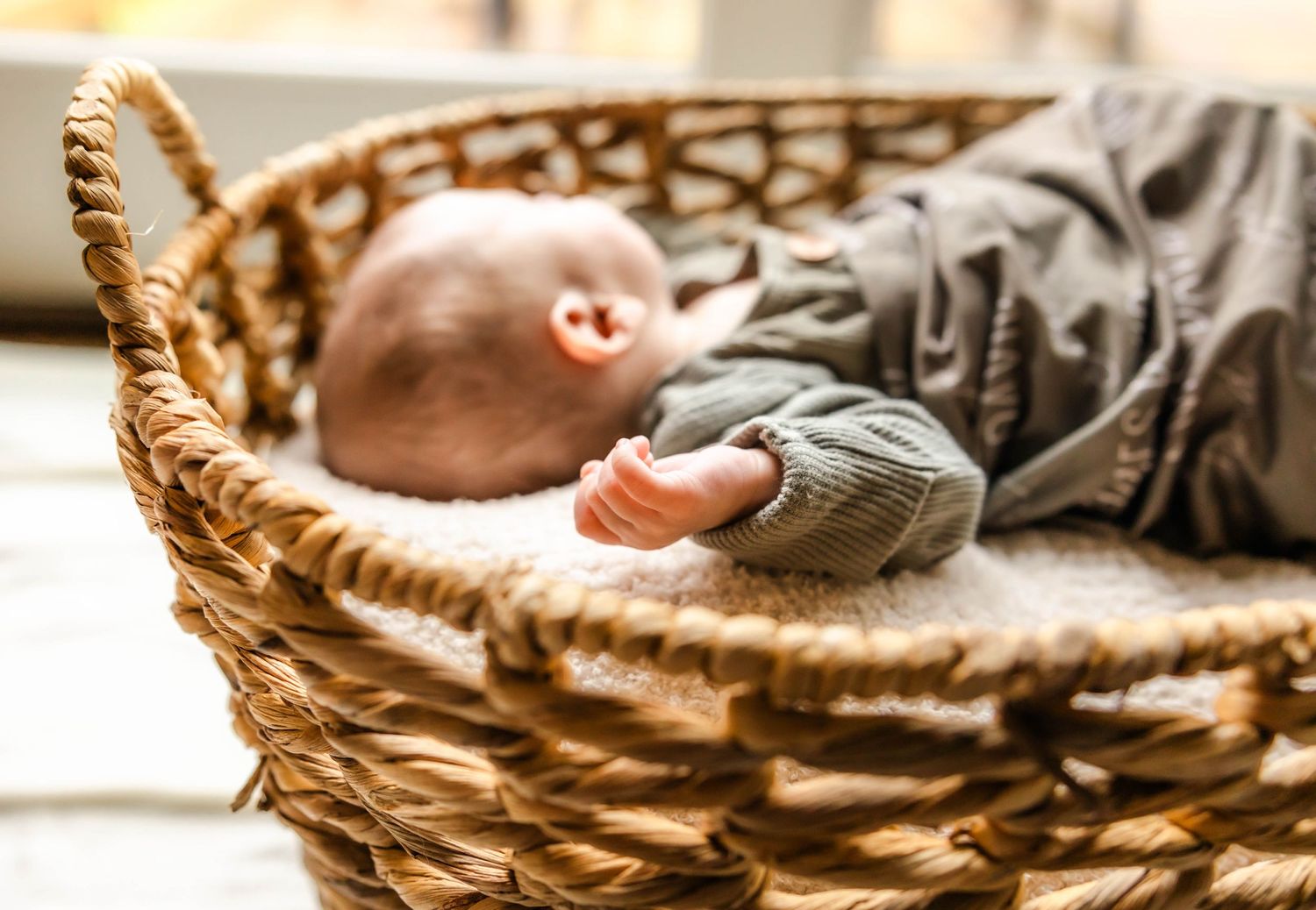 A baby sleeping in a cozy wicker basket wearing gray clothing.