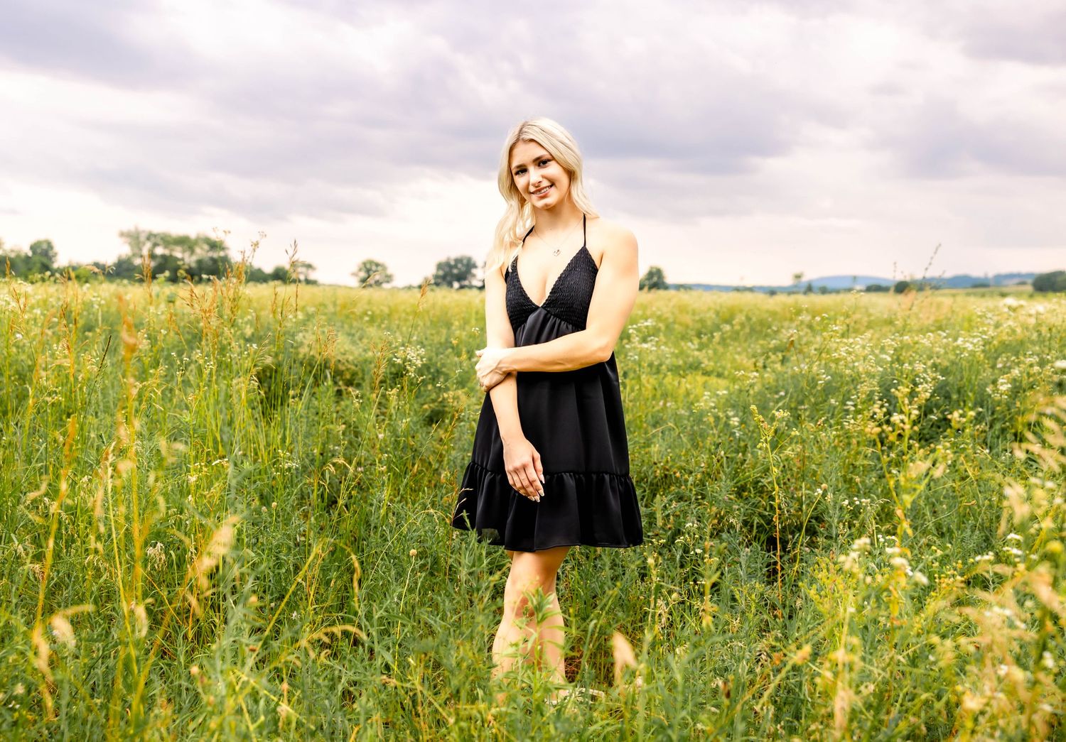 Summer fashion photoshoot featuring a black dress in a rustic field setting.