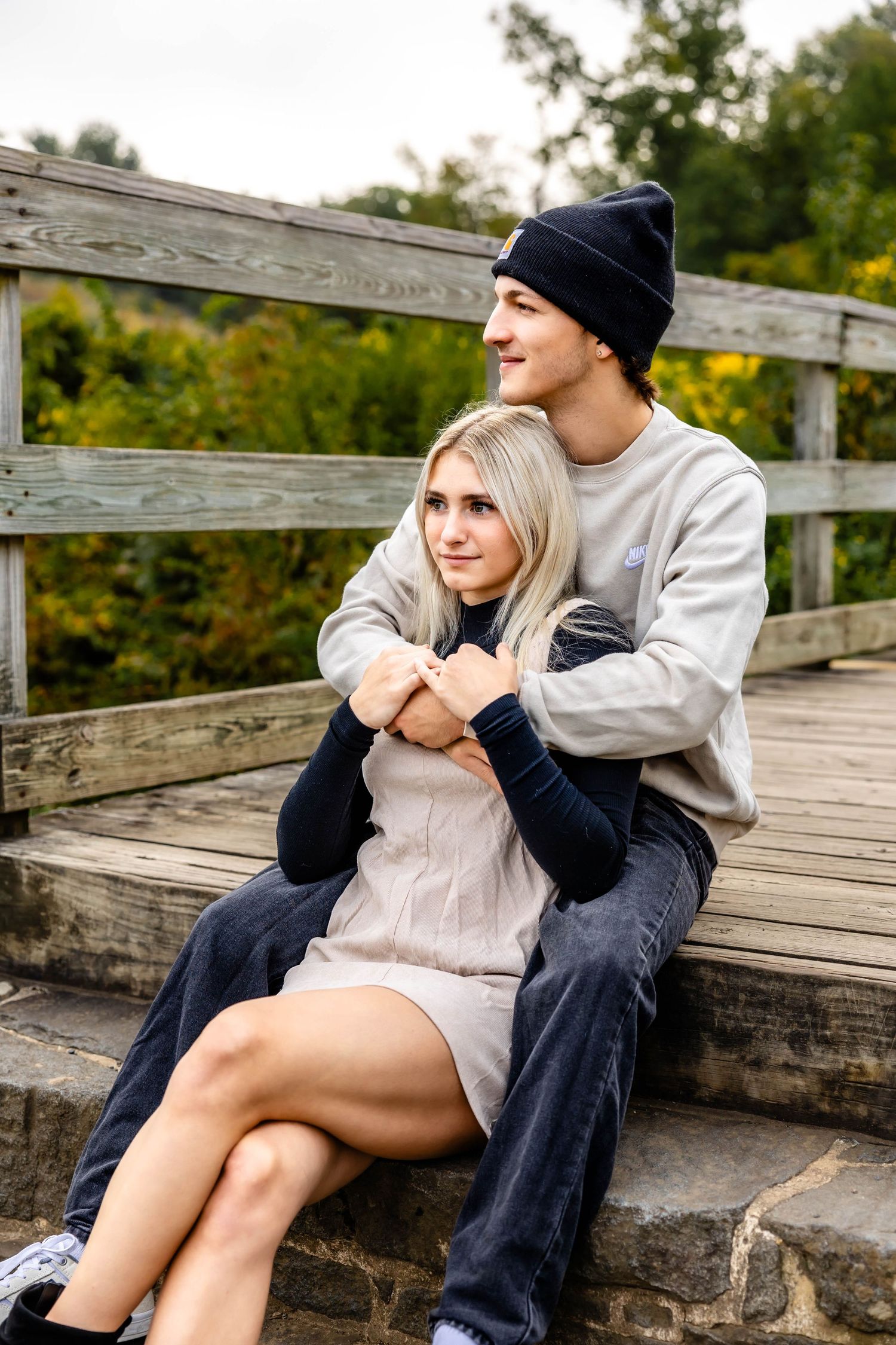 Couple in warm clothing embraces on wooden bridge steps during fall photoshoot.
