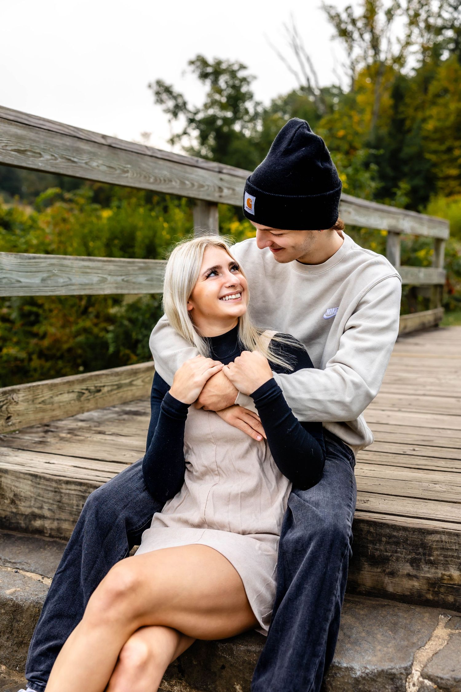 A couple laughs together while sitting on wooden stairs in nature.