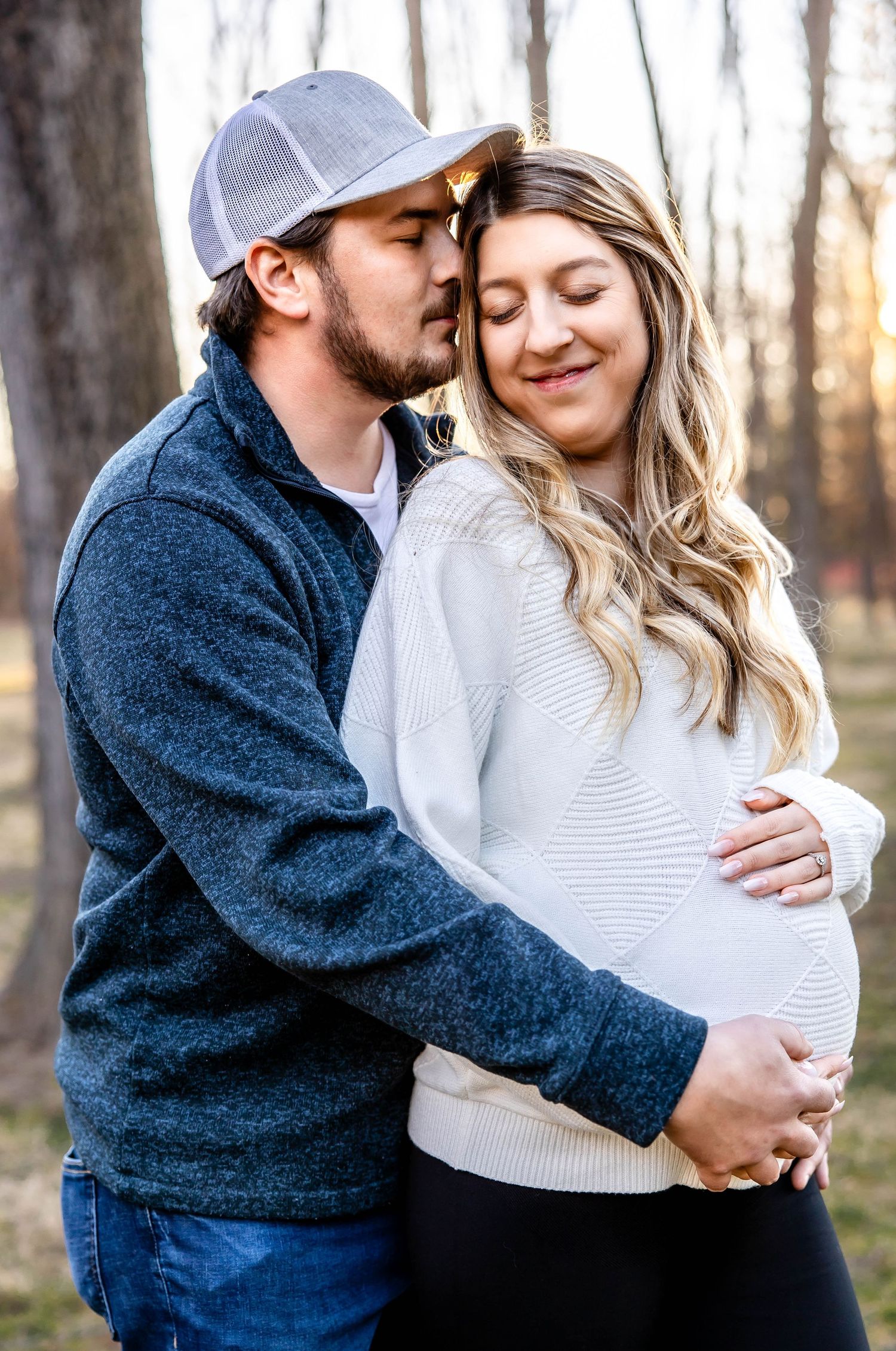 Intimate maternity moment between couple in a forest setting during golden hour.