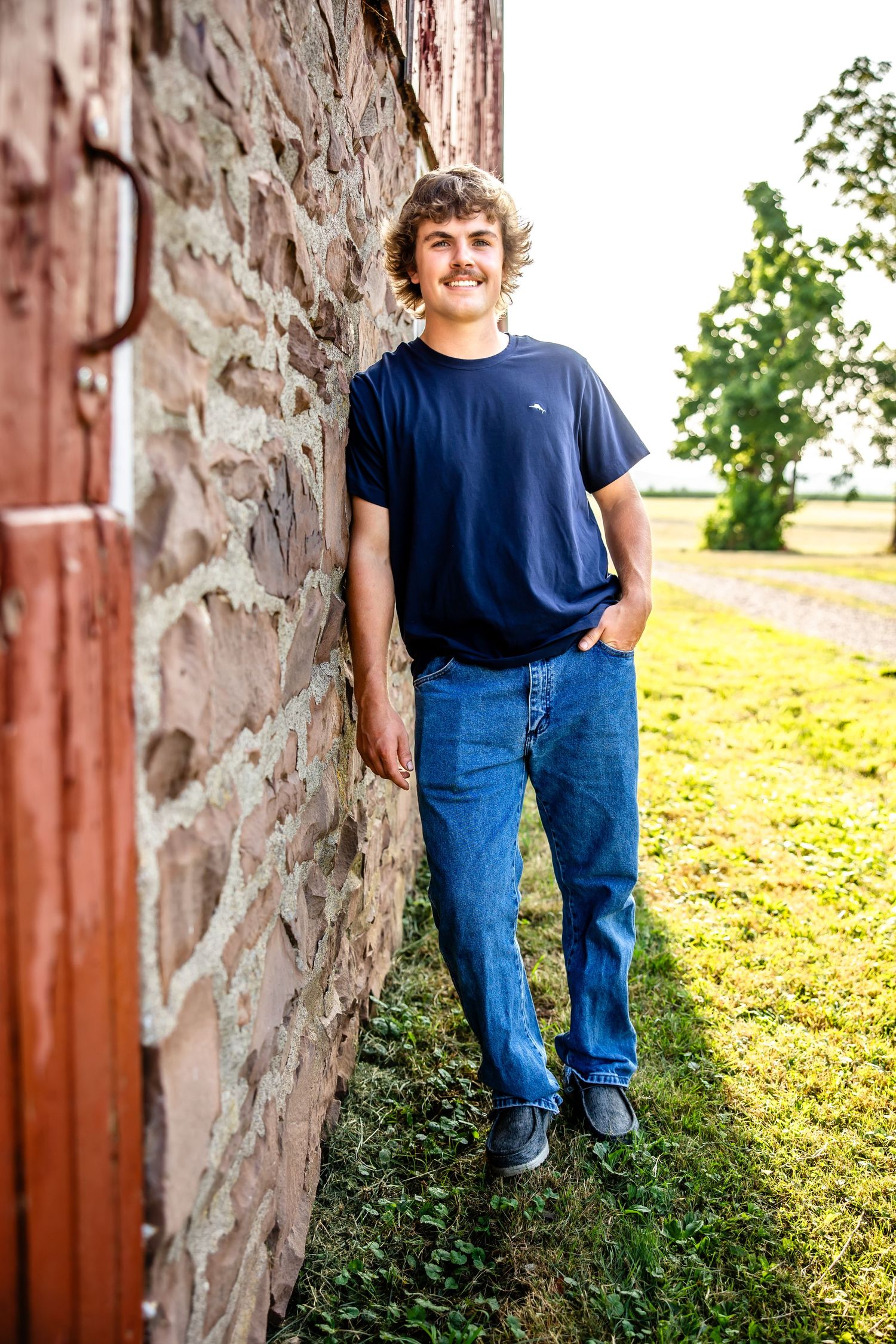 Casual portrait against rustic stone wall wearing navy t-shirt and jeans.