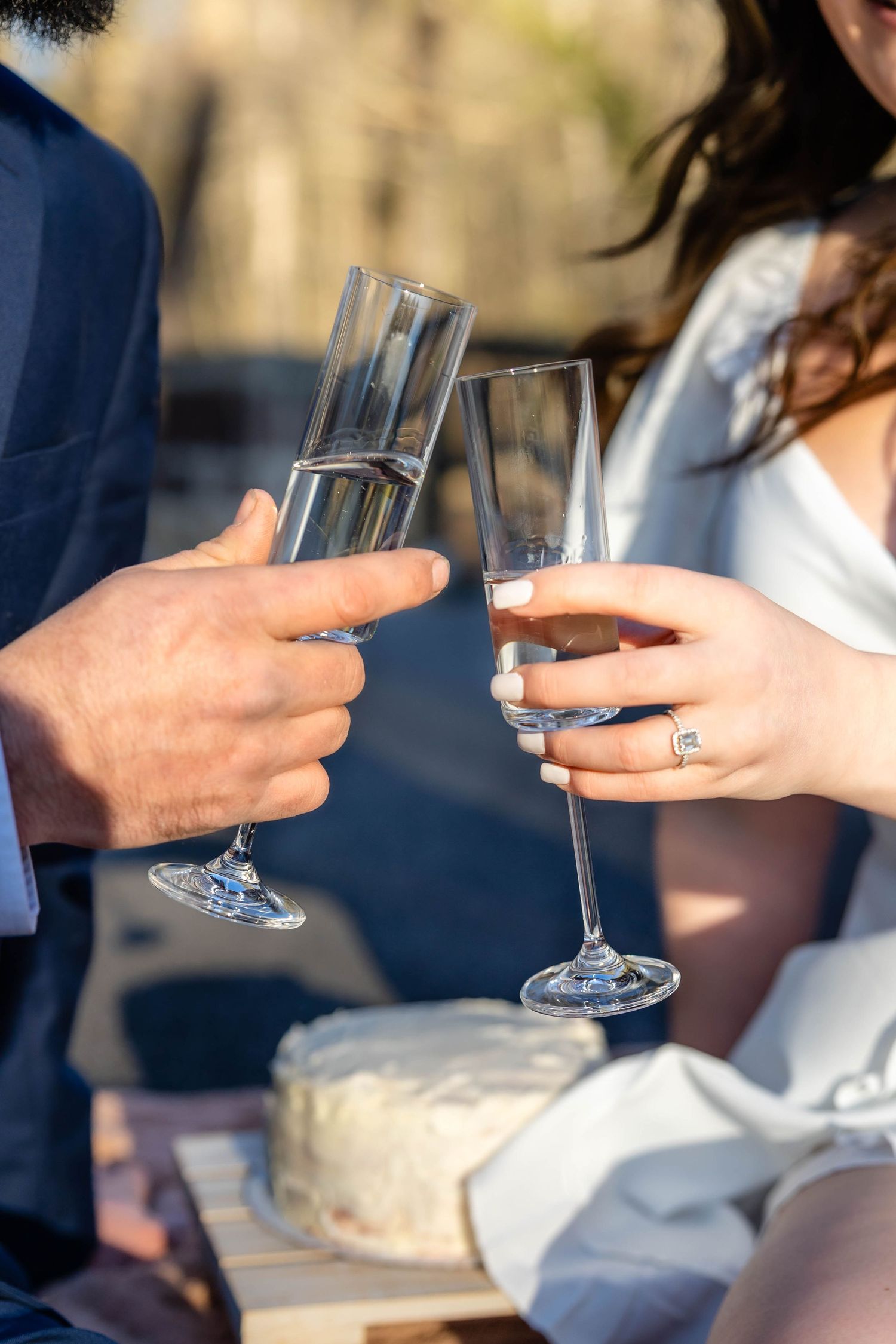 Close-up of champagne glasses clinking with an elegant white cake in the background.