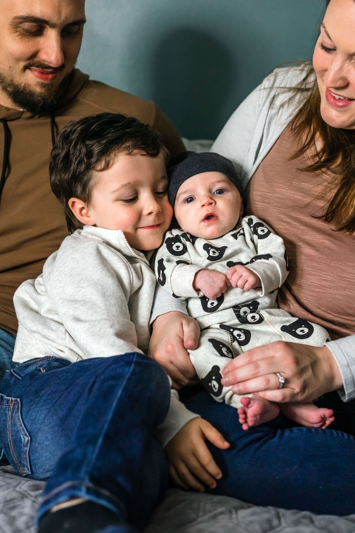 Cozy family moment on couch showing toddler bonding with baby sibling in panda print onesie.