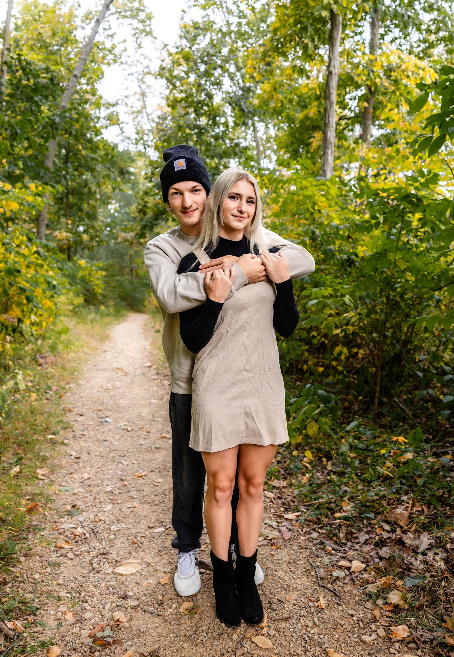 A couple shares a playful moment while posing on a leaf-covered forest trail.