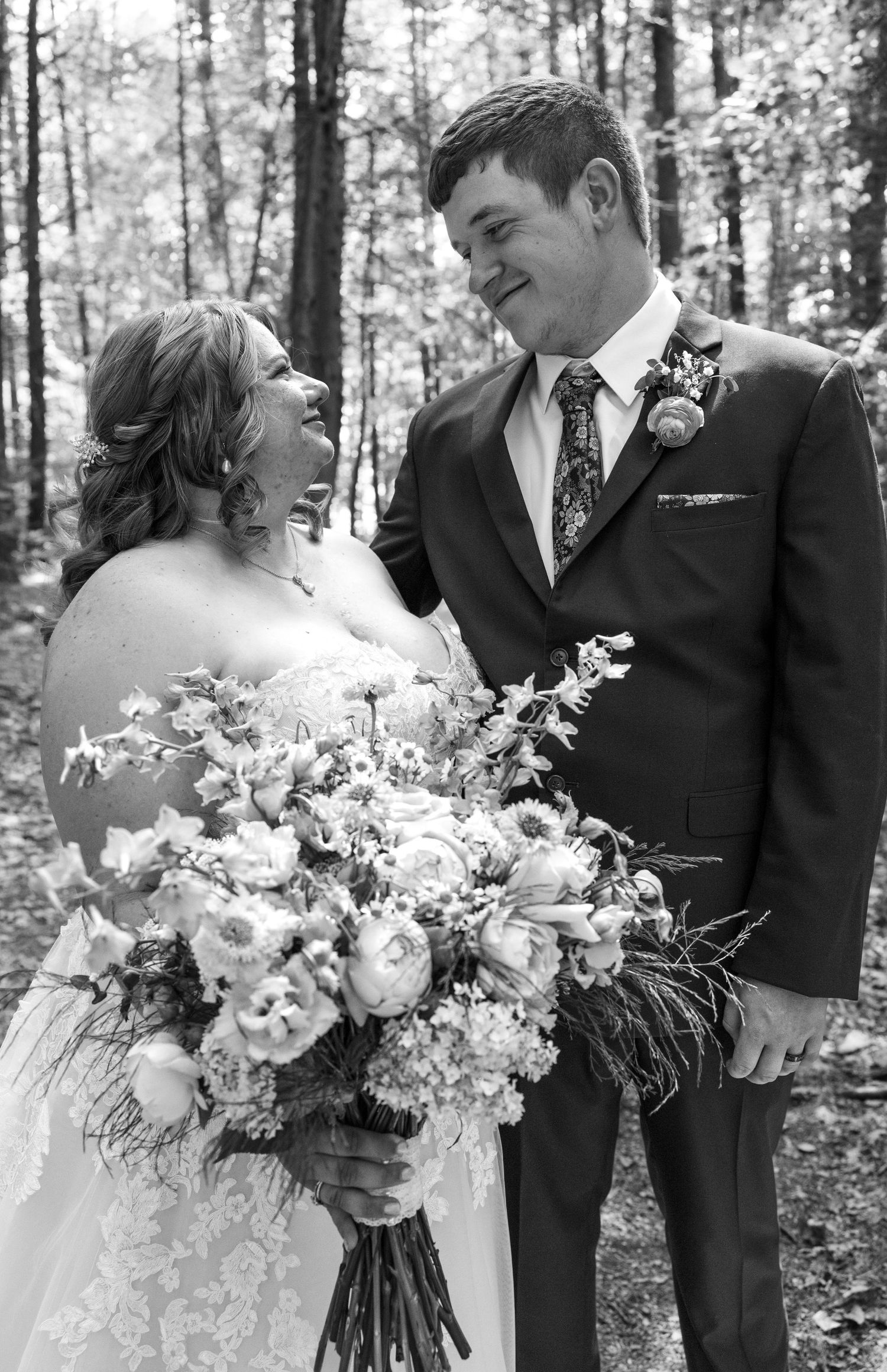 A candid wedding photo in a forest setting with flowers and joyful expressions.