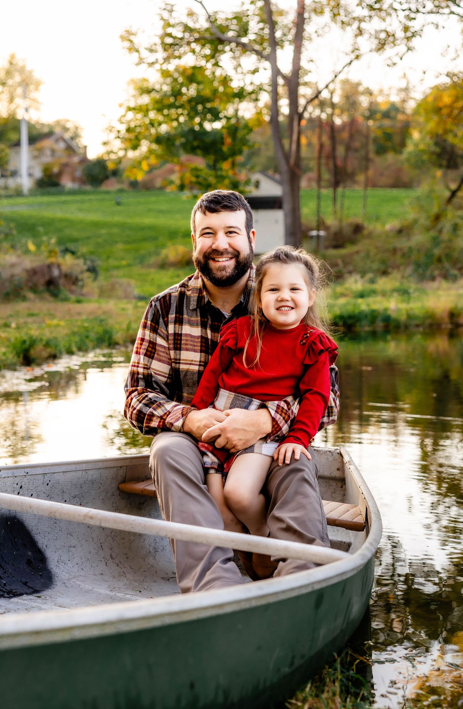 A pair sits together in a canoe during a sunny autumn afternoon by the water.