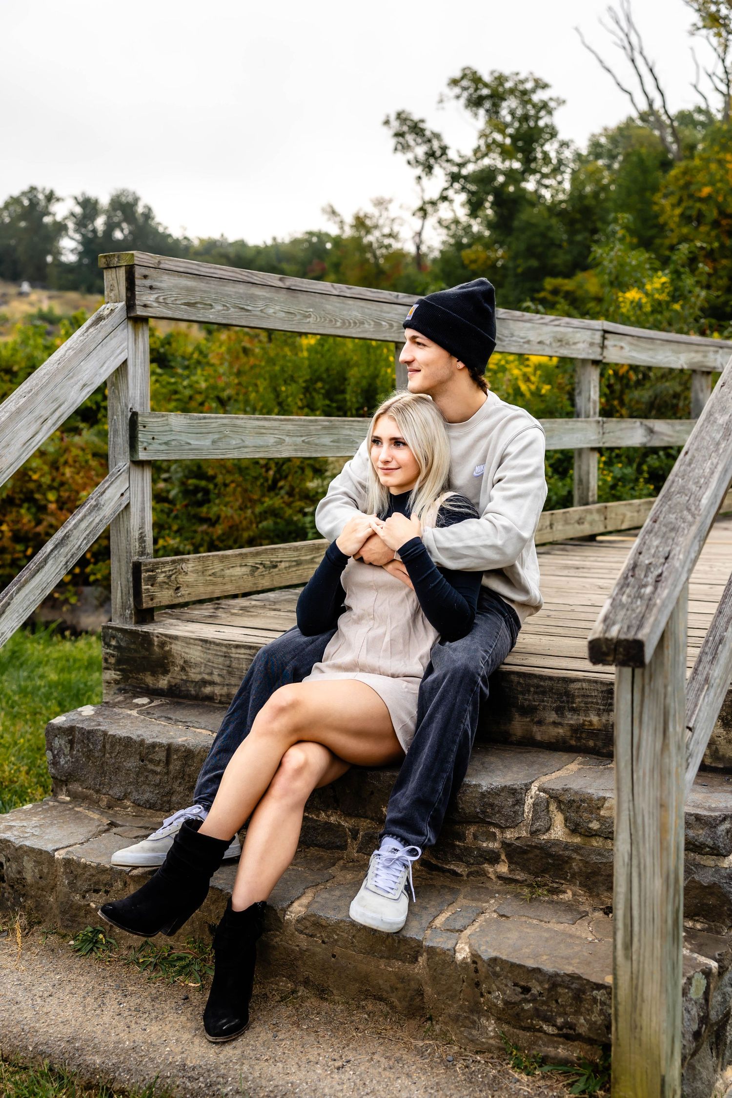 A couple sits together on rustic steps surrounded by fall foliage.