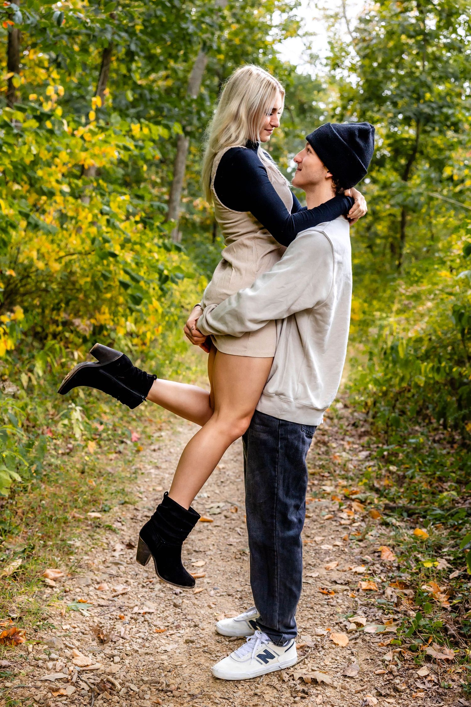 A playful couple embracing on a forest trail with golden autumn foliage in the background.