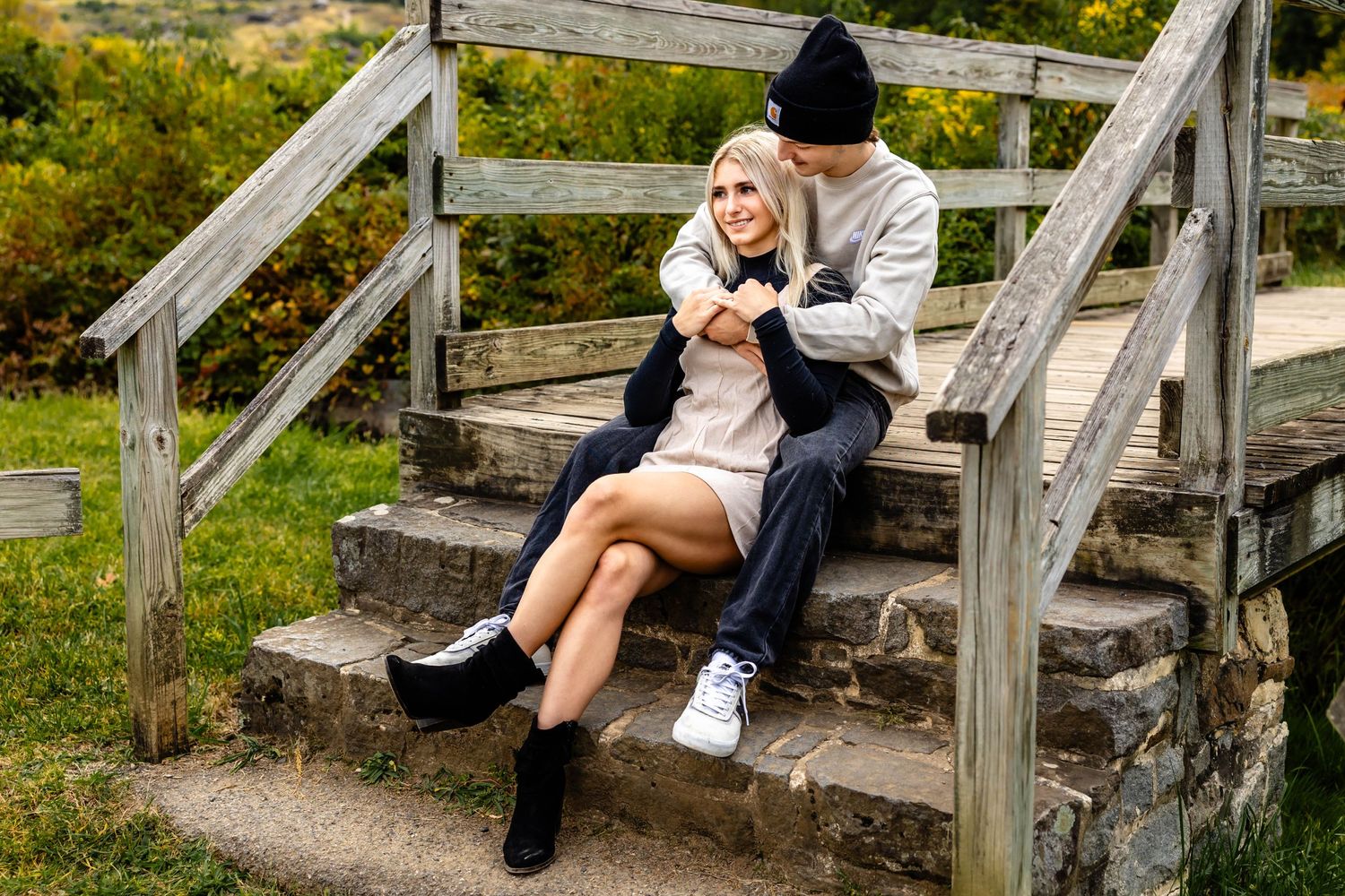 Romantic couple sitting on wooden steps against autumn landscape backdrop.