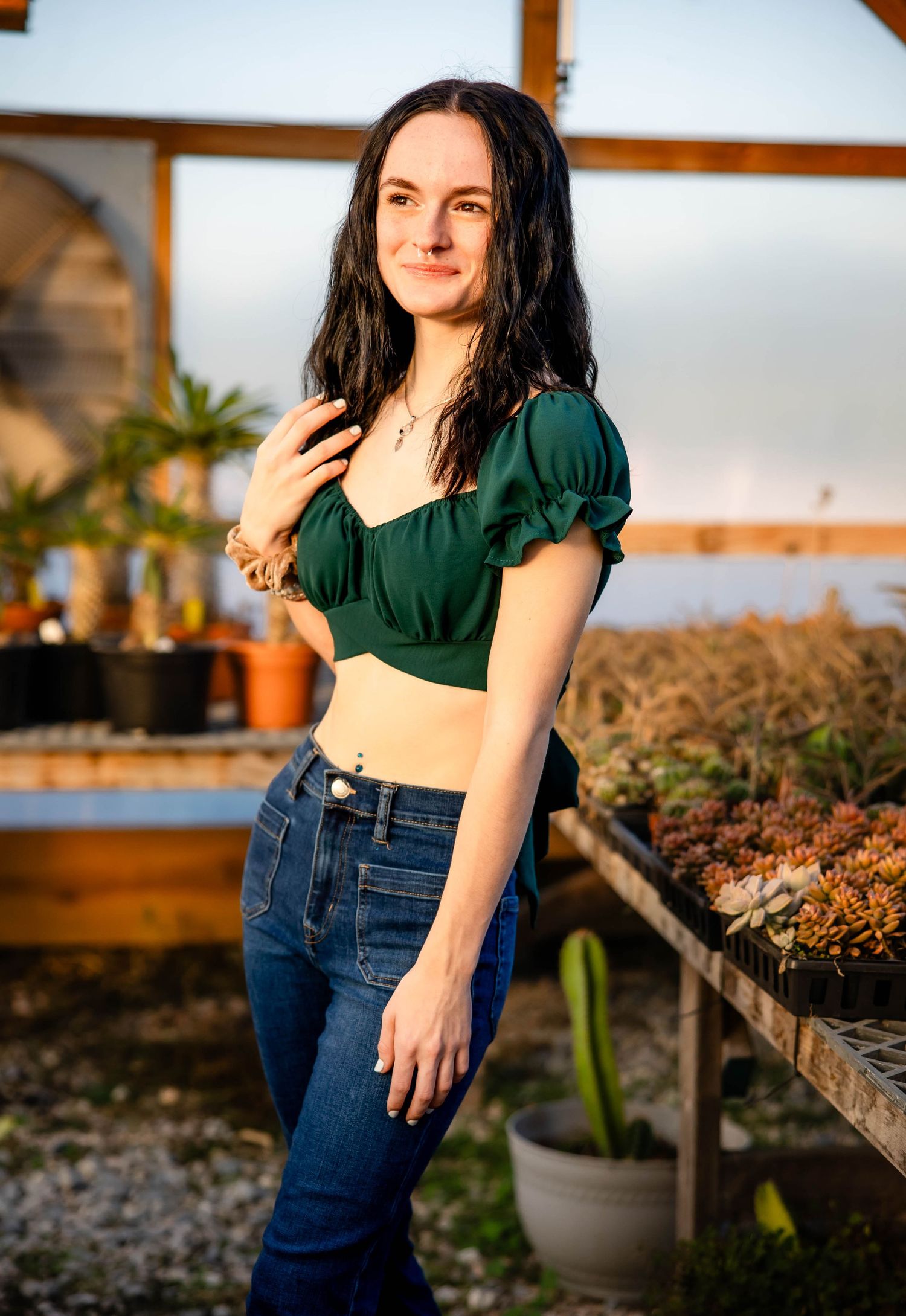 Sunset portrait in a greenhouse wearing dark green top and denim.
