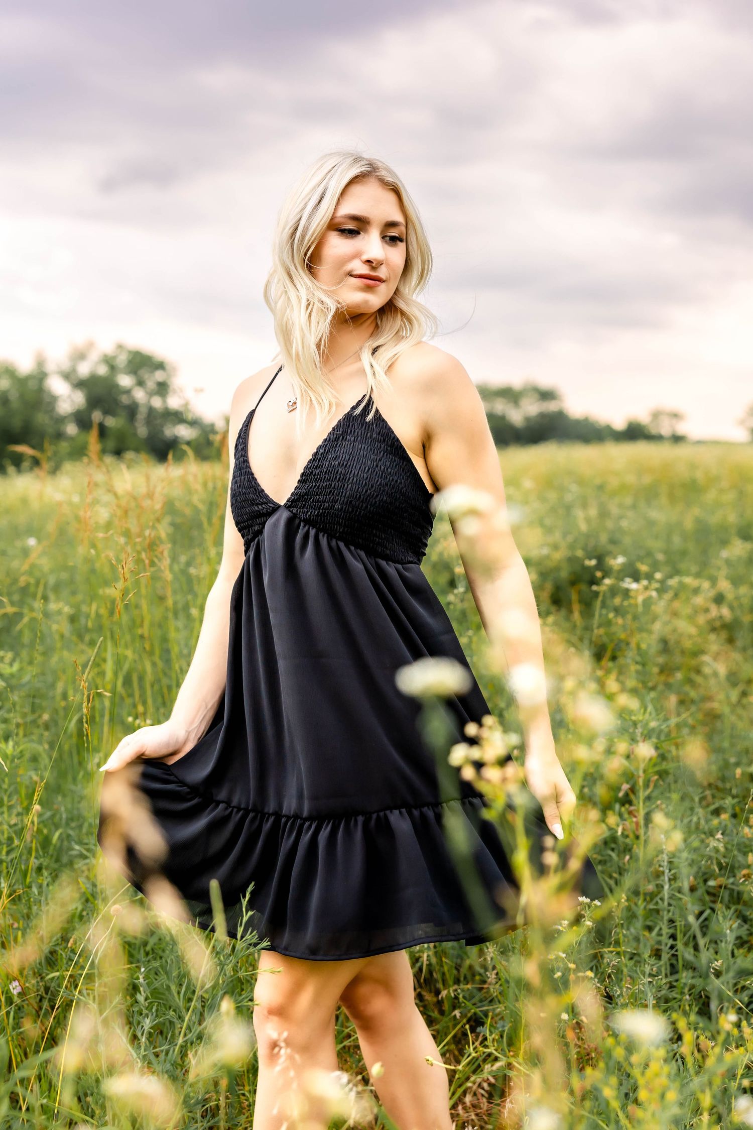 Black empire waist dress with ruffle detail shown among tall grasses and wildflowers.