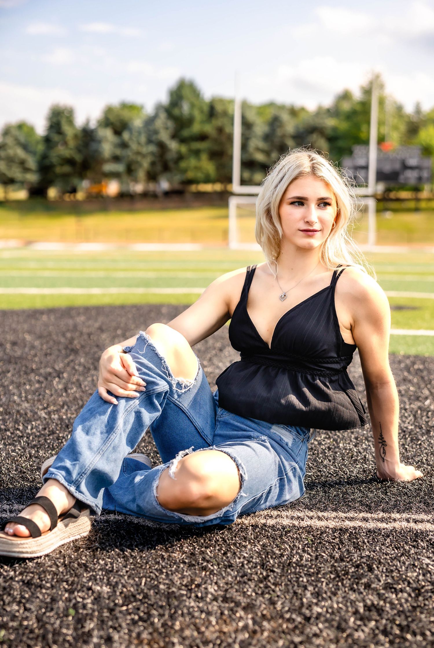 Athletic field portrait showing casual summer style with distressed denim and black top.