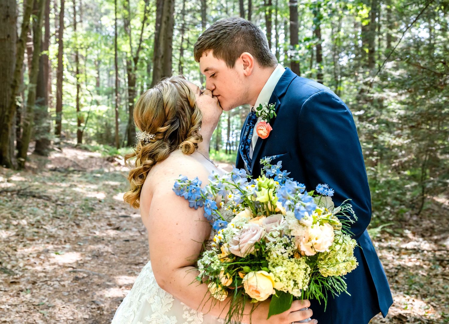 Intimate wedding portrait of couple sharing romantic moment with floral bouquet in woods.