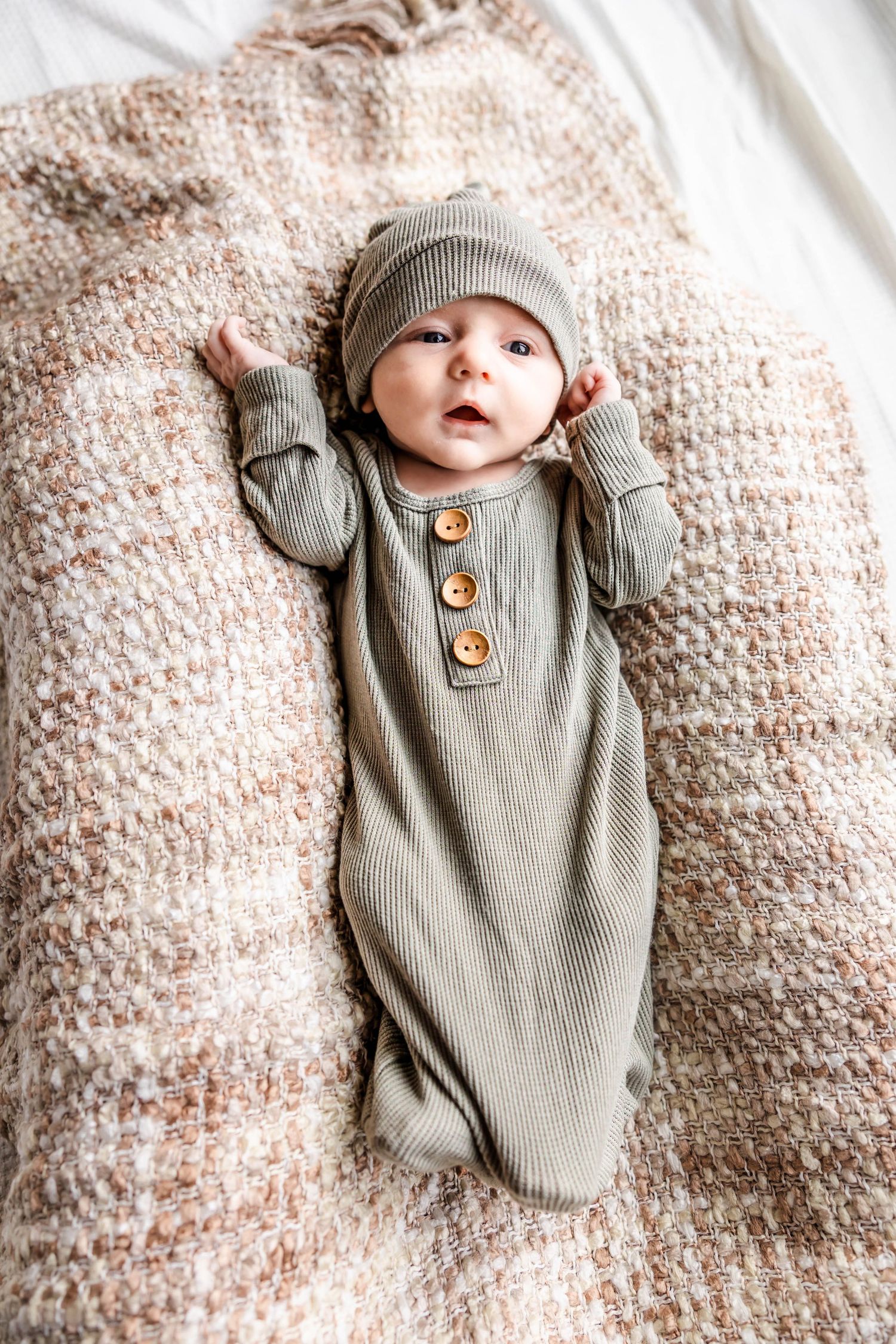 Infant in grey ribbed sleeper and matching hat resting on knit blanket.