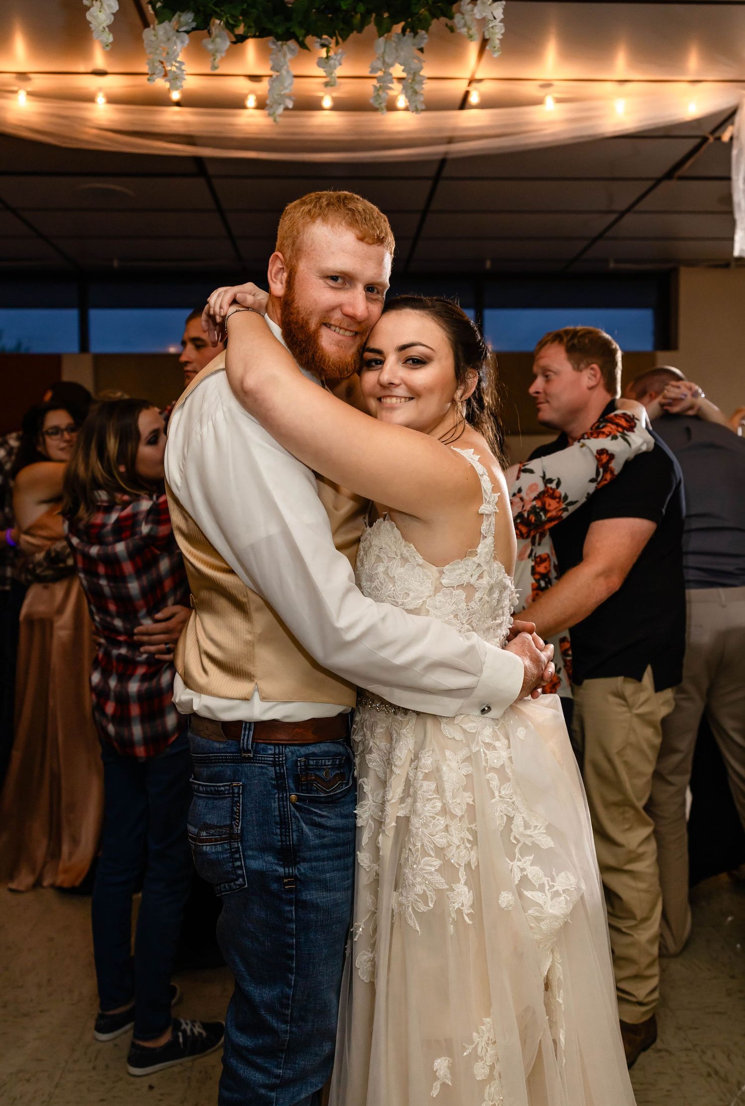 A couple embraces on their wedding dance floor under decorative string lights.